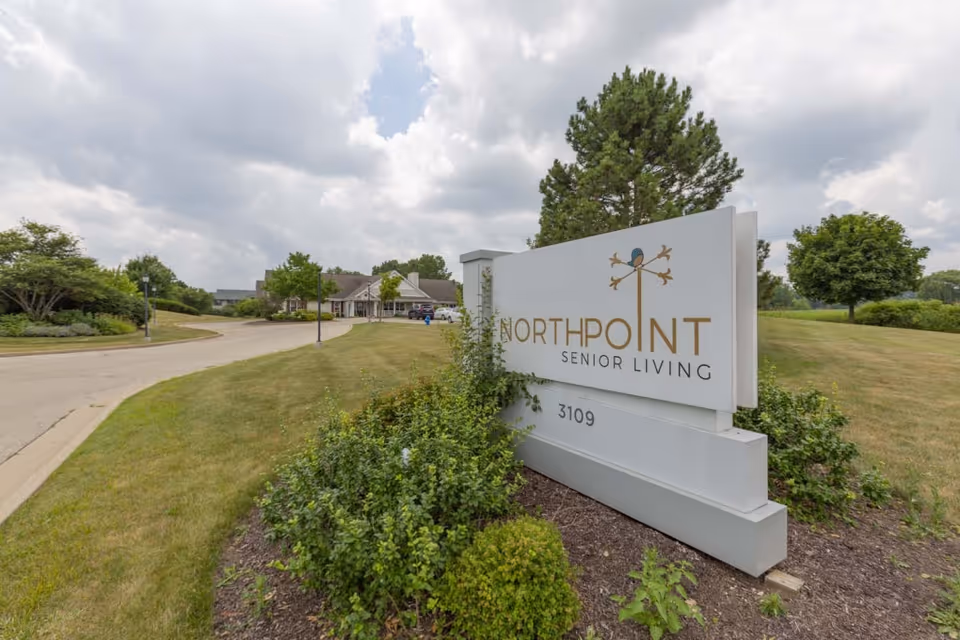 Entrance sign reading 'NorthPoint Senior Living' beside a driveway with the facility and landscaping in the background.
