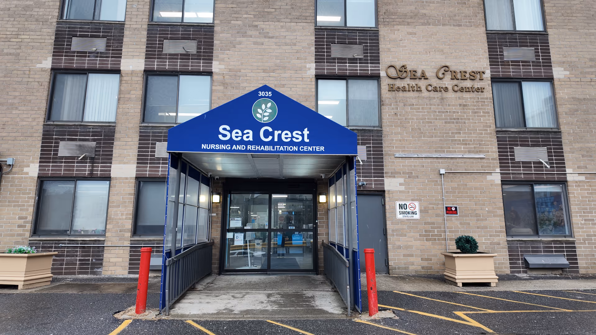 Front entrance of a brick nursing and rehabilitation building with a blue canopy reading 'Sea Crest'.