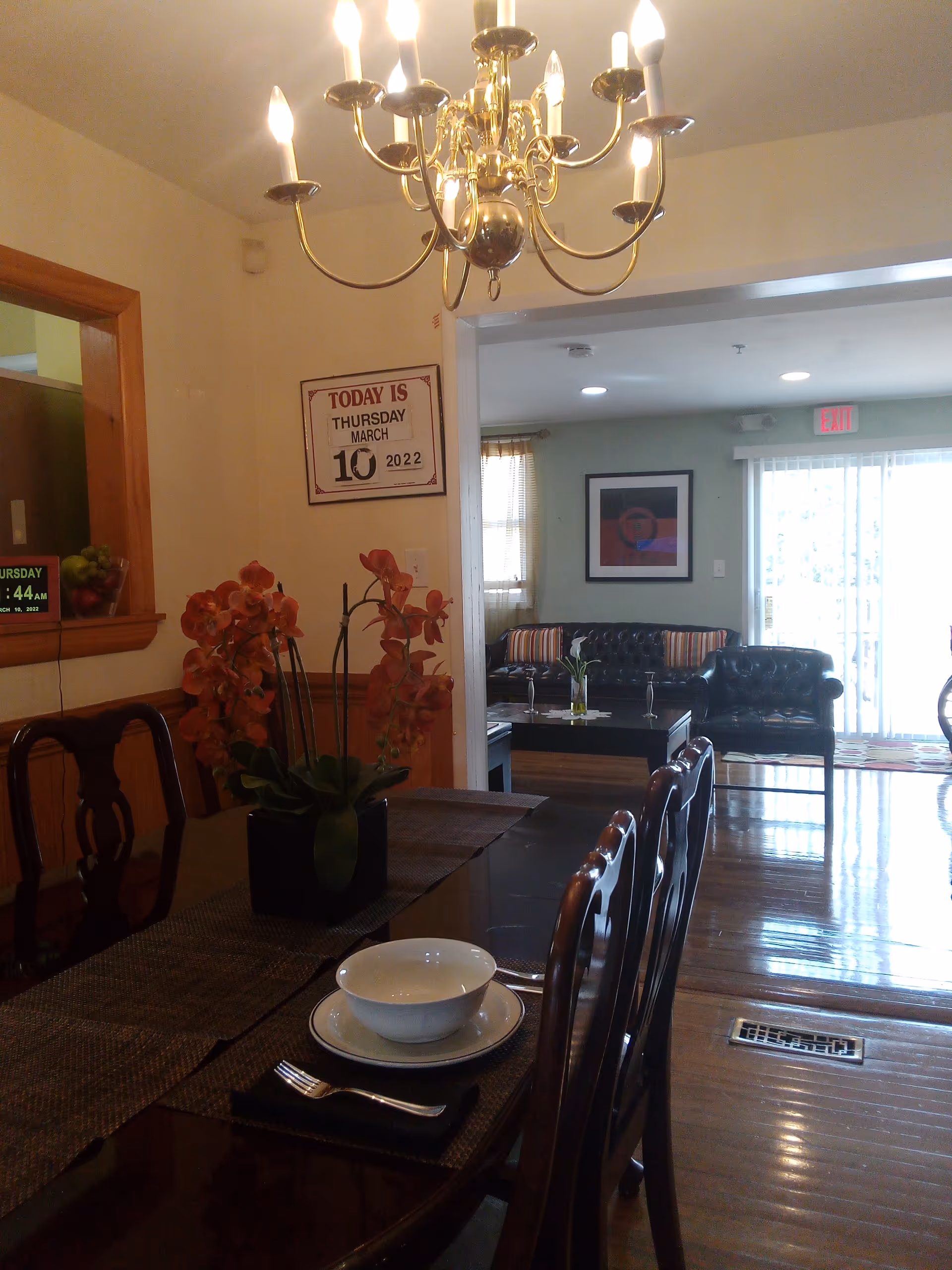 A dining room with a chandelier, long table set for meals, and a living area beyond.