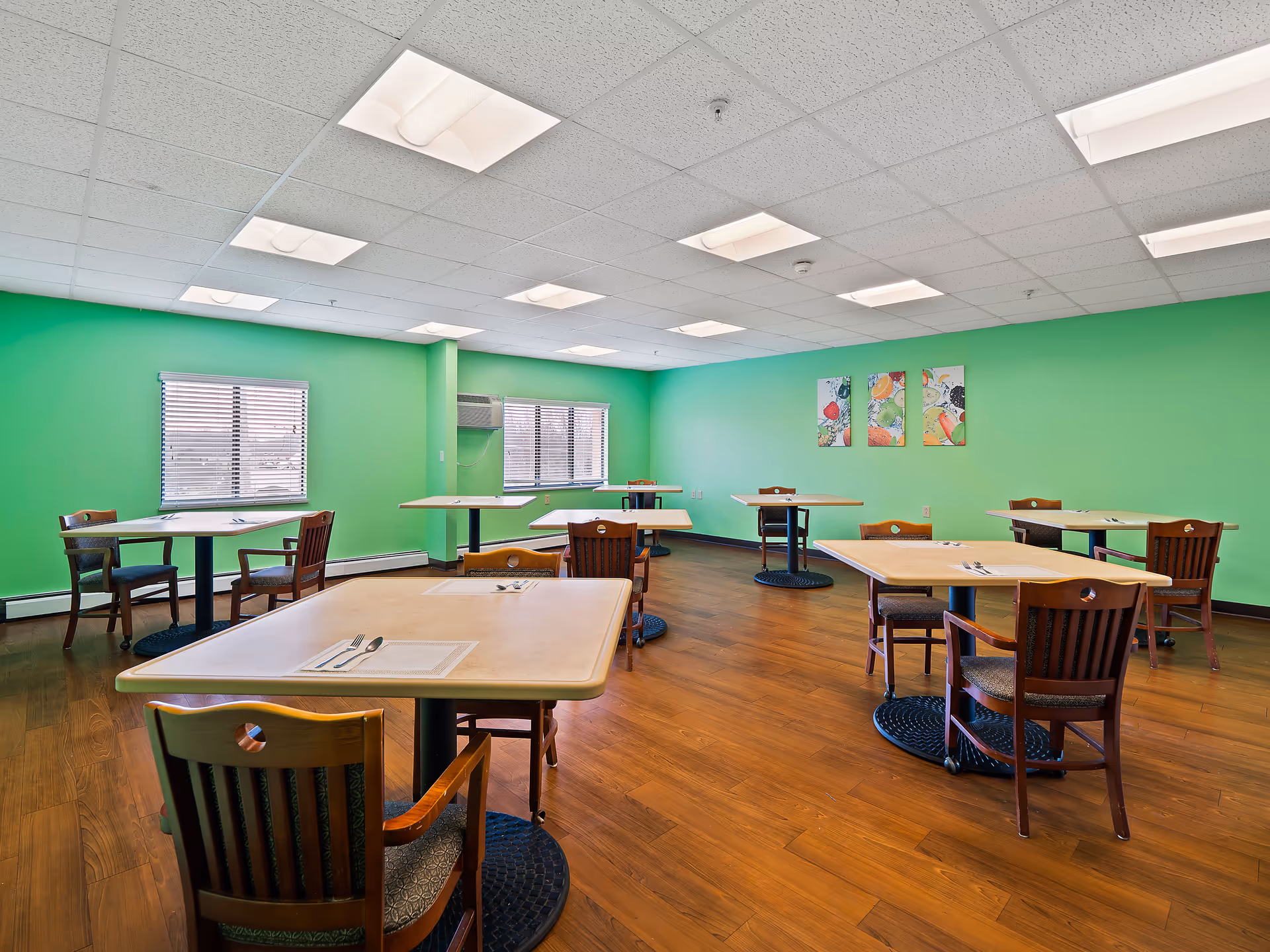 Bright green dining room with several empty tables and wooden chairs in a senior facility