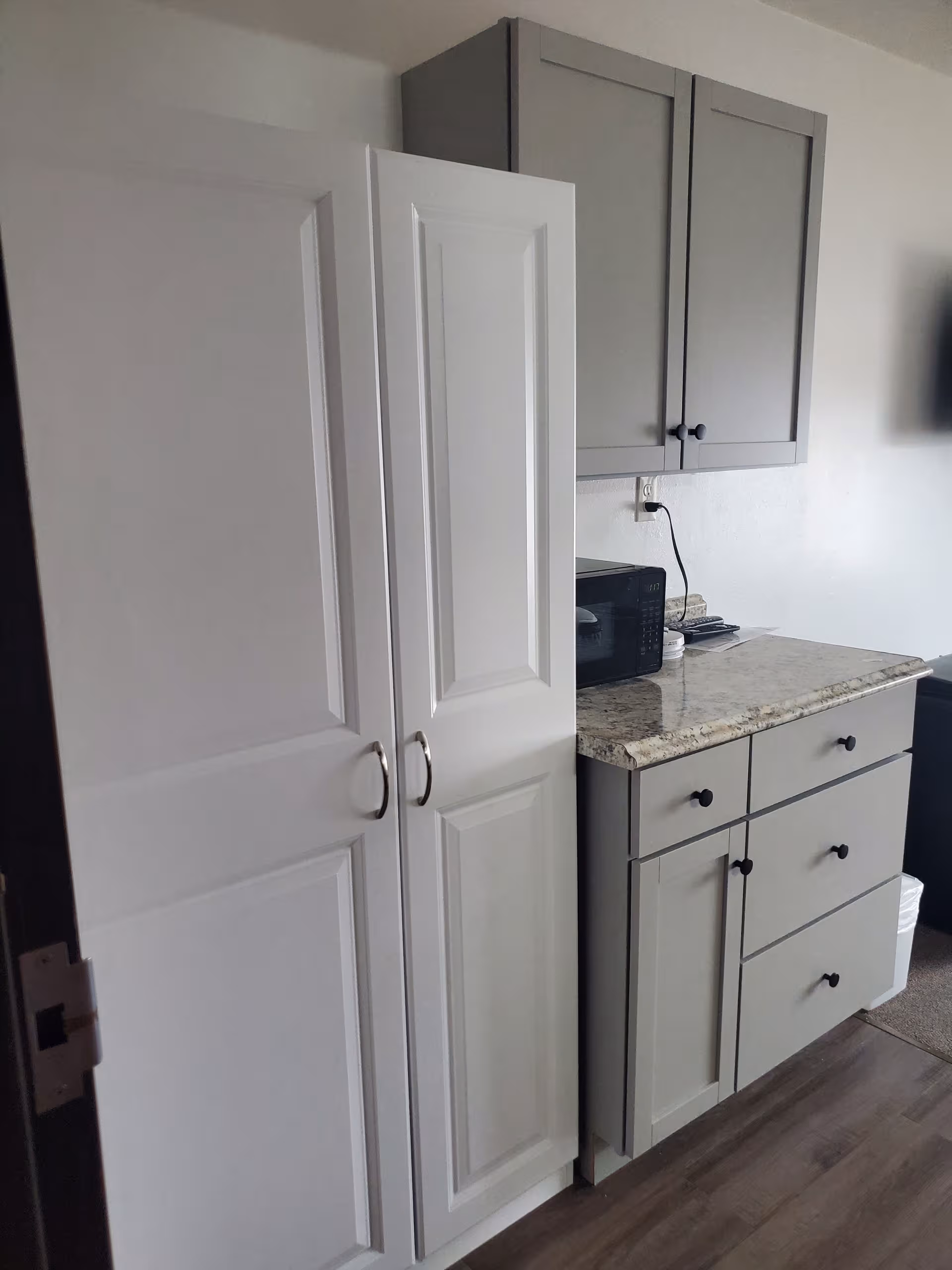 Compact kitchen with white pantry doors, gray cabinets, granite countertop, and a microwave.