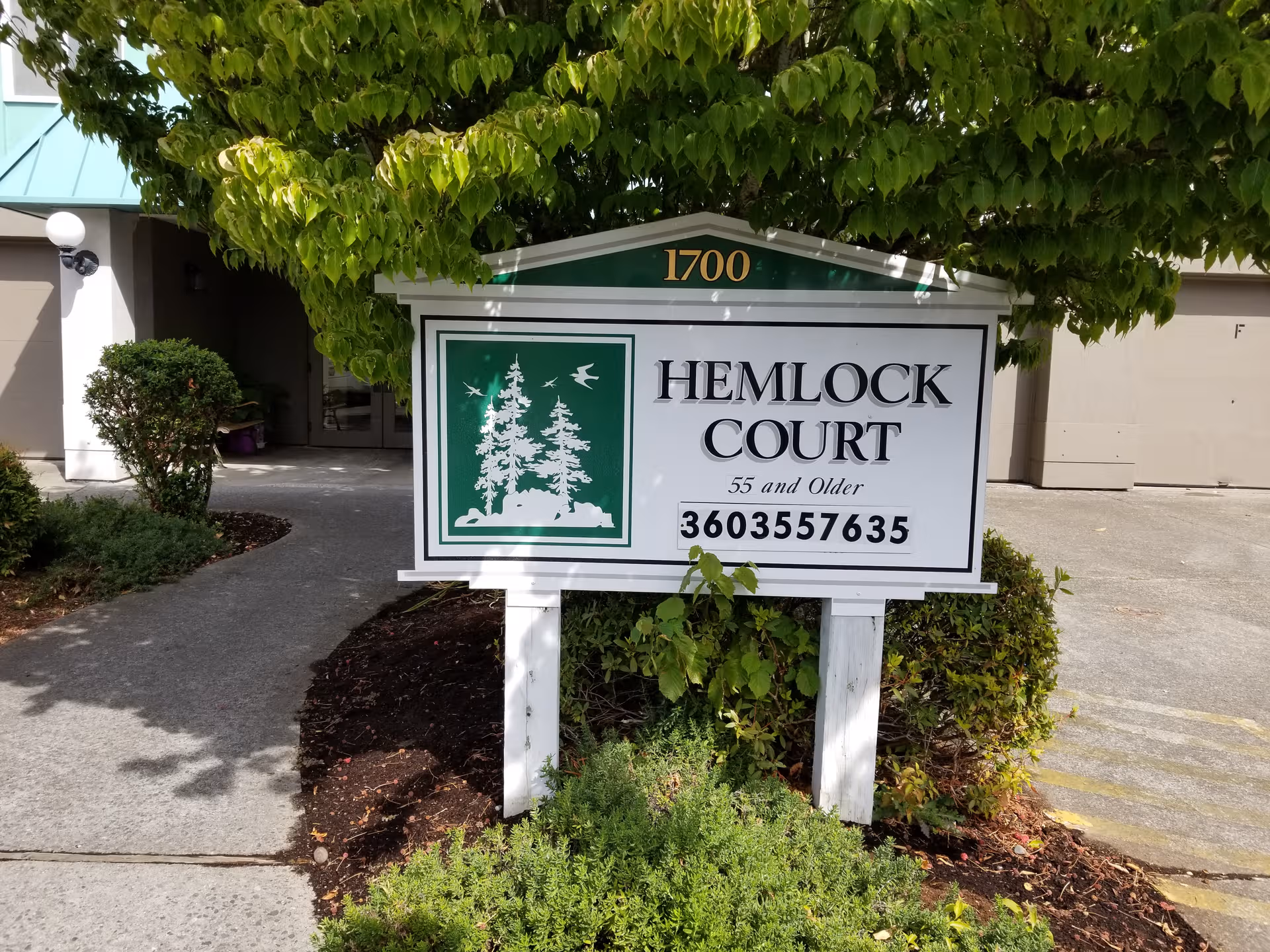 Hemlock Court sign at the building's front entrance with greenery and driveway.