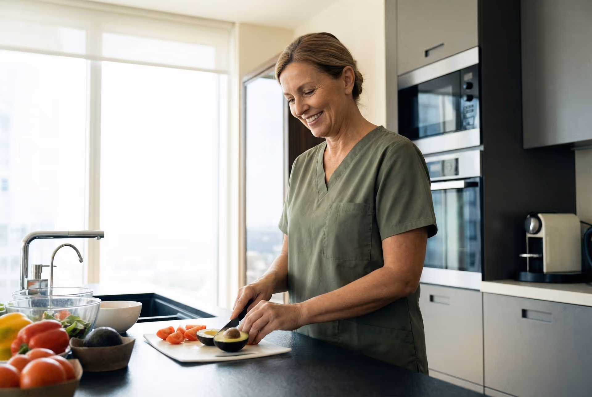 Caregiver in scrubs chops vegetables at a modern kitchen counter.