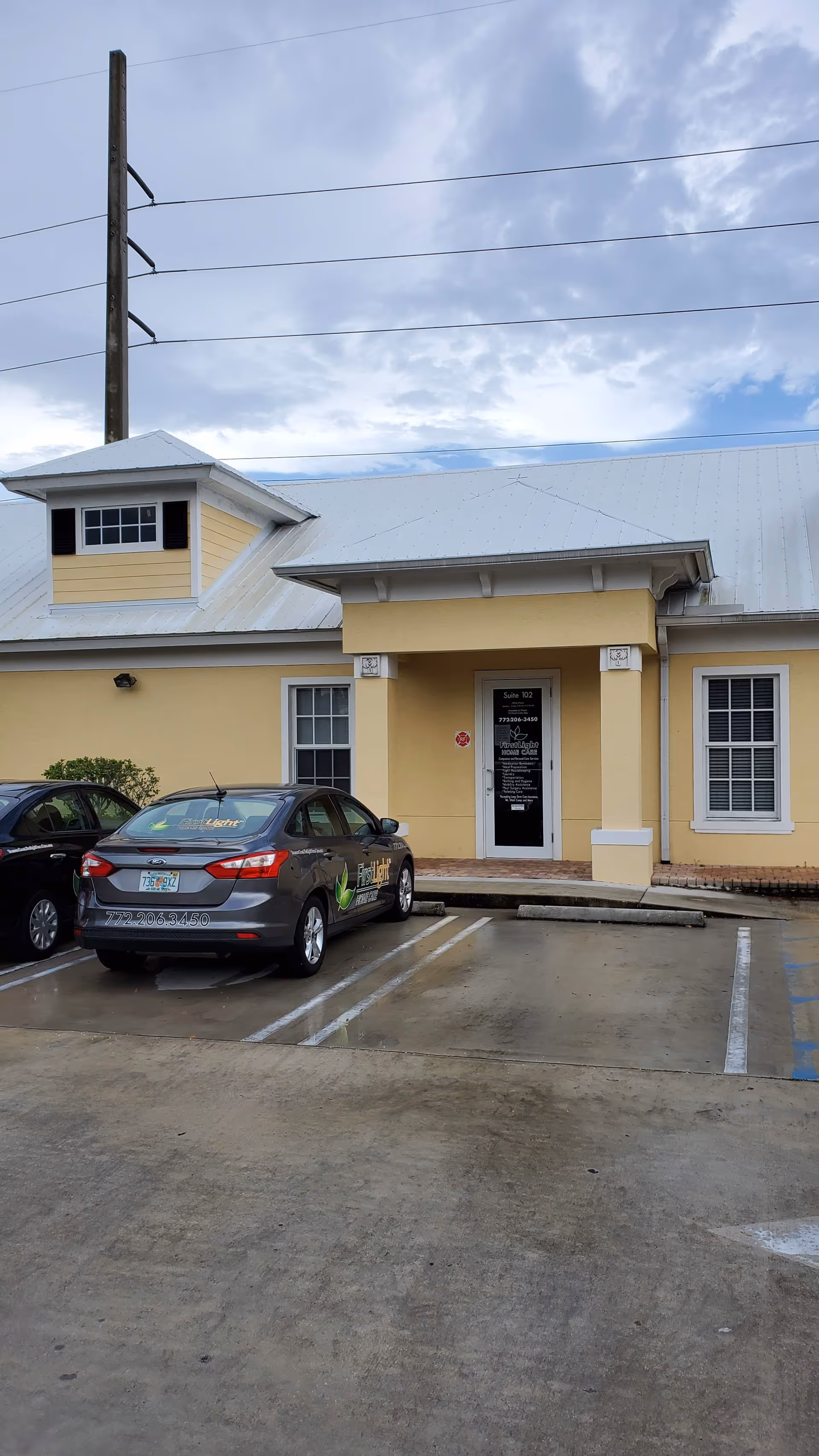 Yellow senior care facility exterior with entrance, parked cars, and a cloudy sky.
