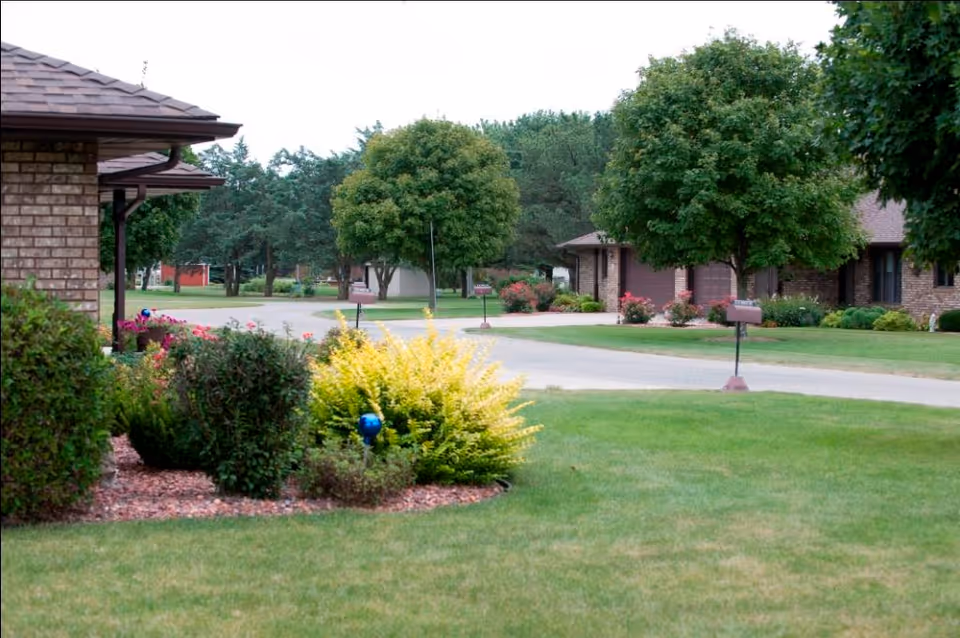 Manicured lawns, shrubs, and trees along a quiet street of single-story brick homes with mailboxes.
