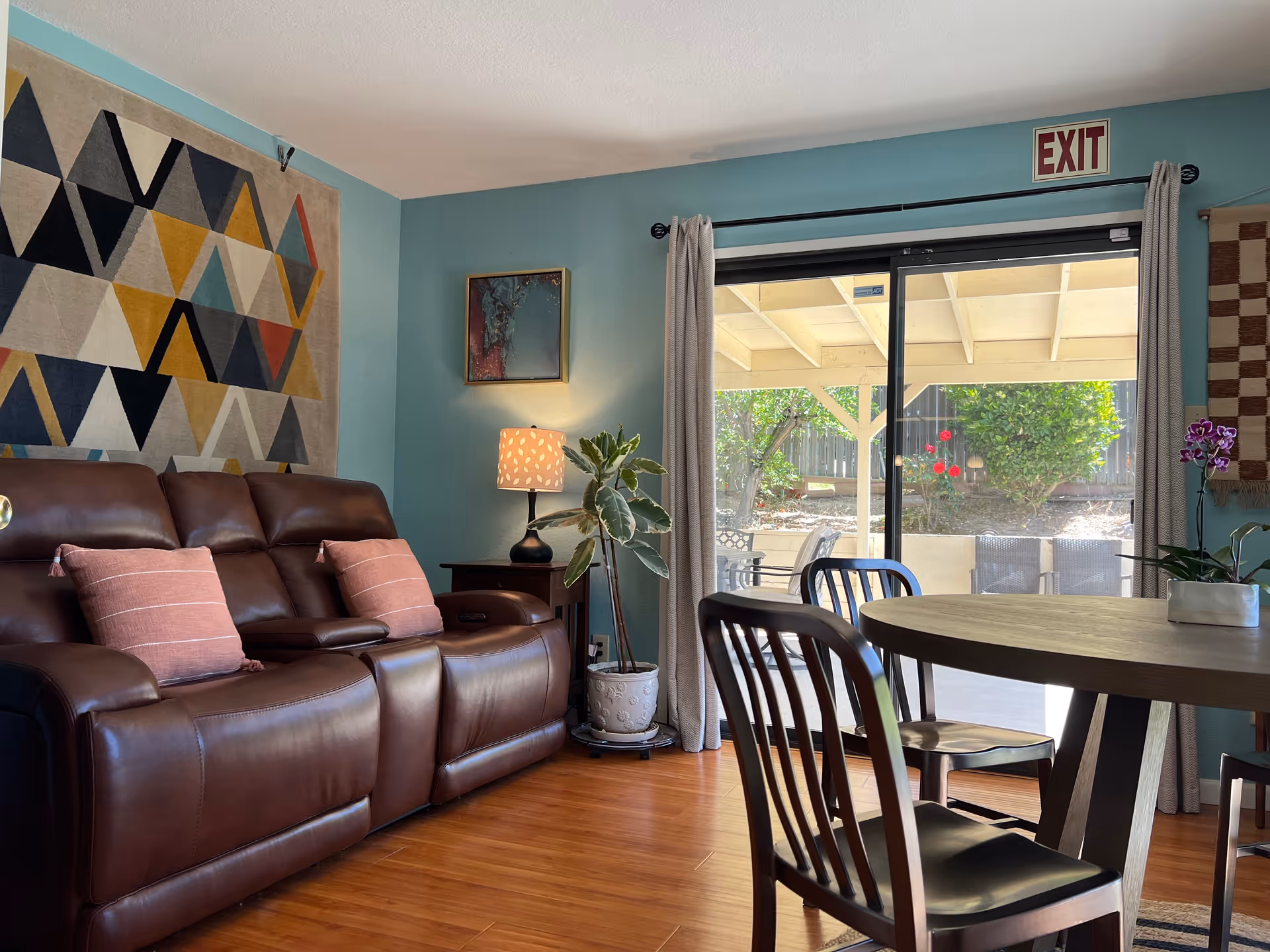 Cozy living room with leather sofa, artwork, plants, and a sliding glass door to the patio.