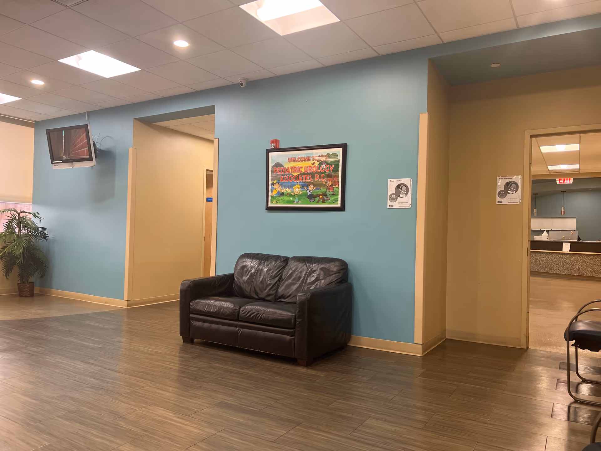 Blue-walled waiting area with a black leather sofa and framed wall art.