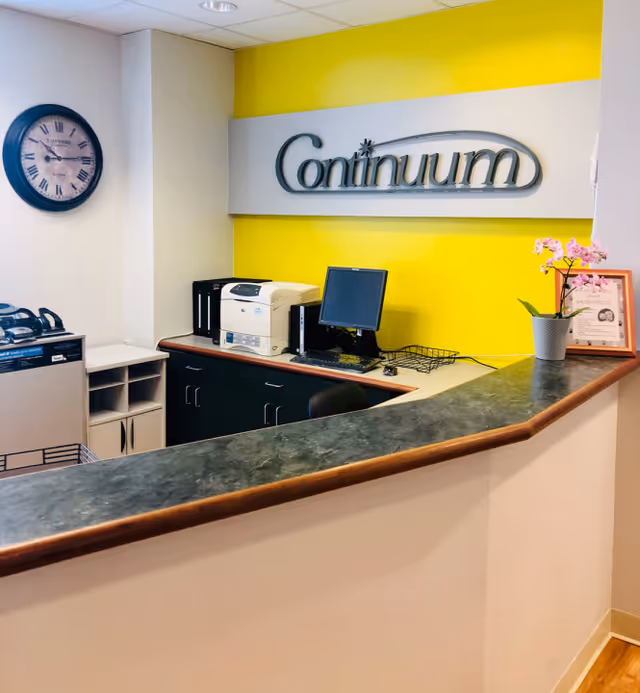 Reception area featuring a yellow wall, Continuum sign, desk, printer, and clock.