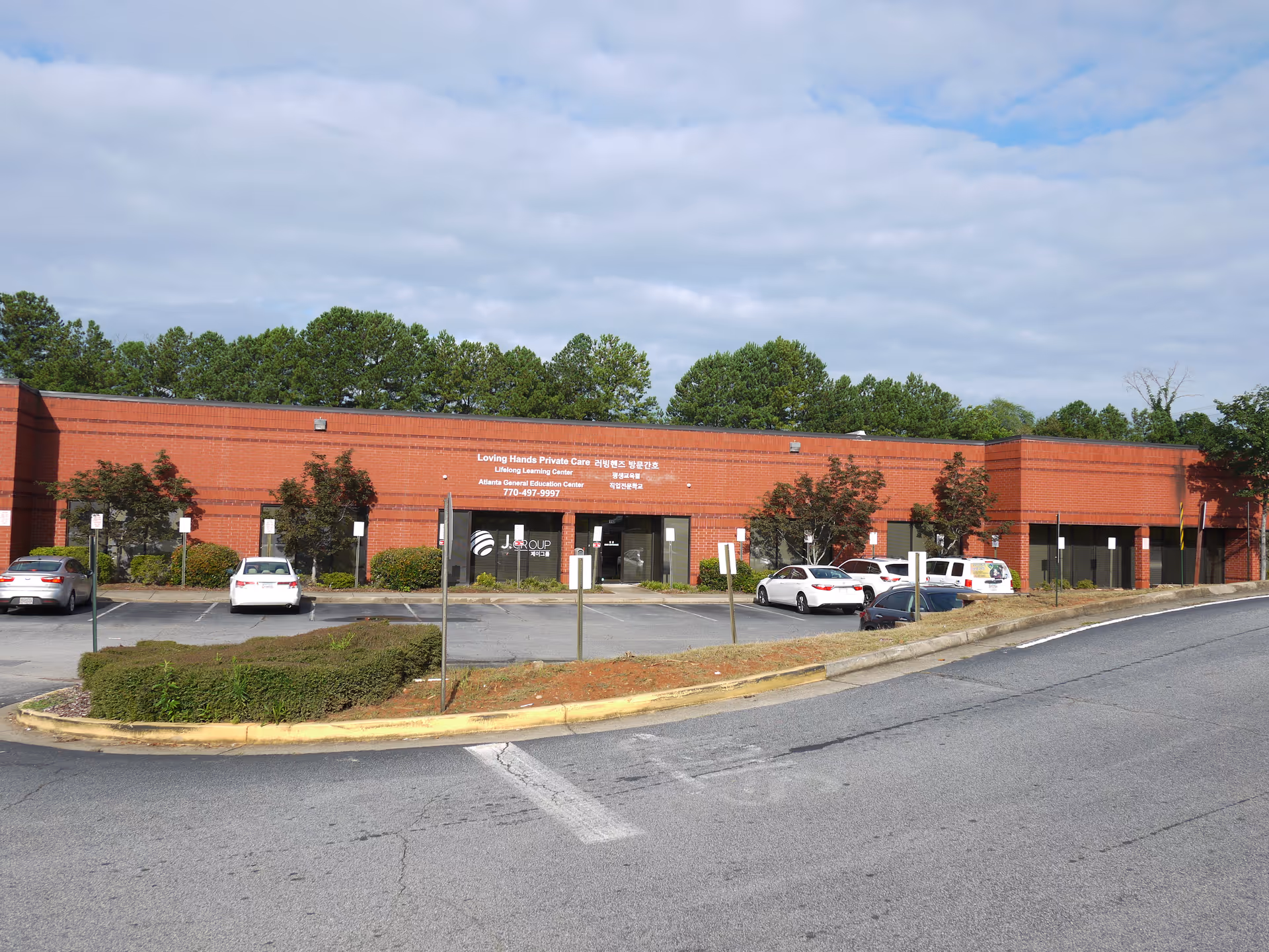 Brick, single-story building with a parking lot in front and trees behind.