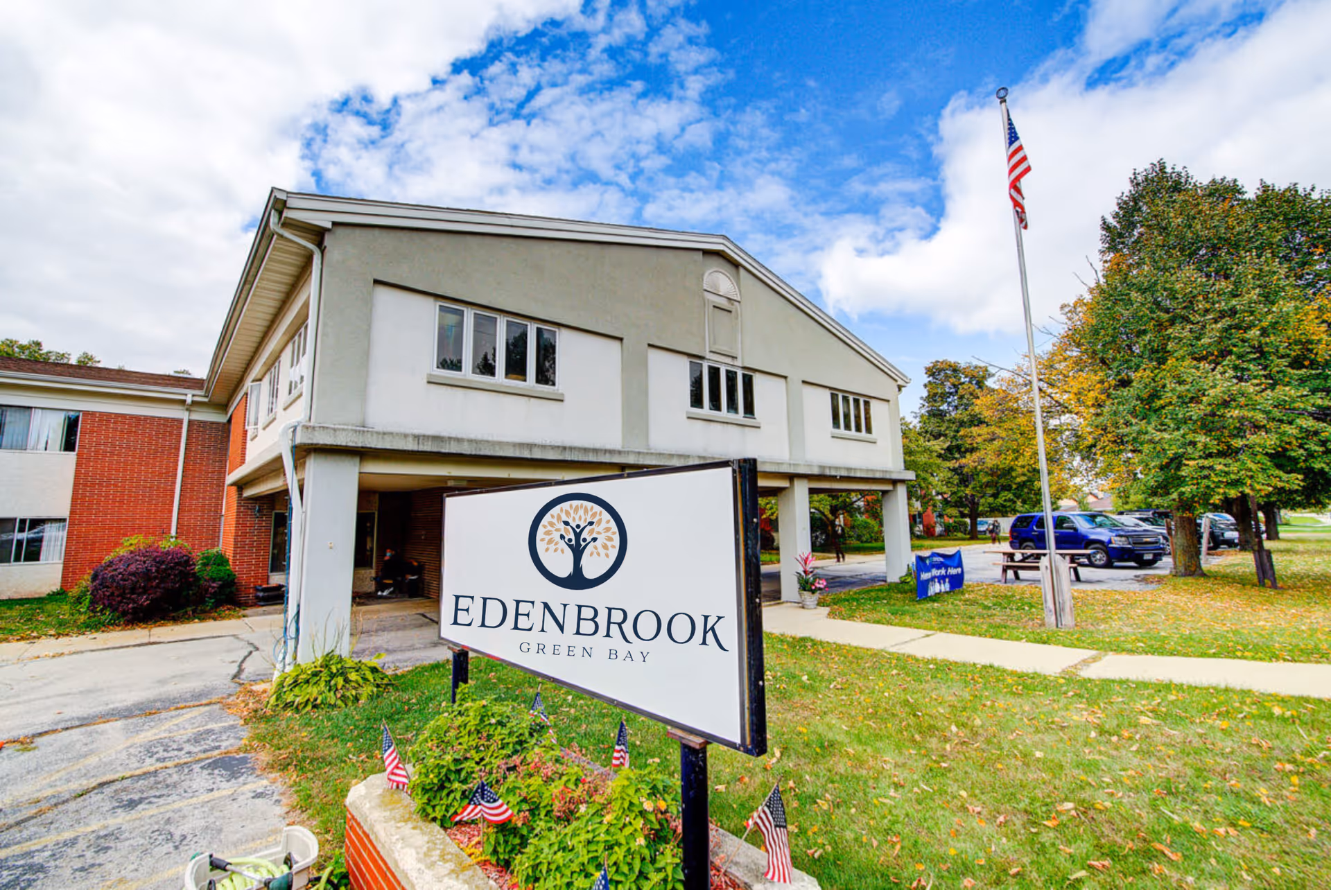 Edenbrook Green Bay senior living facility exterior with sign, flagpole, and cars.