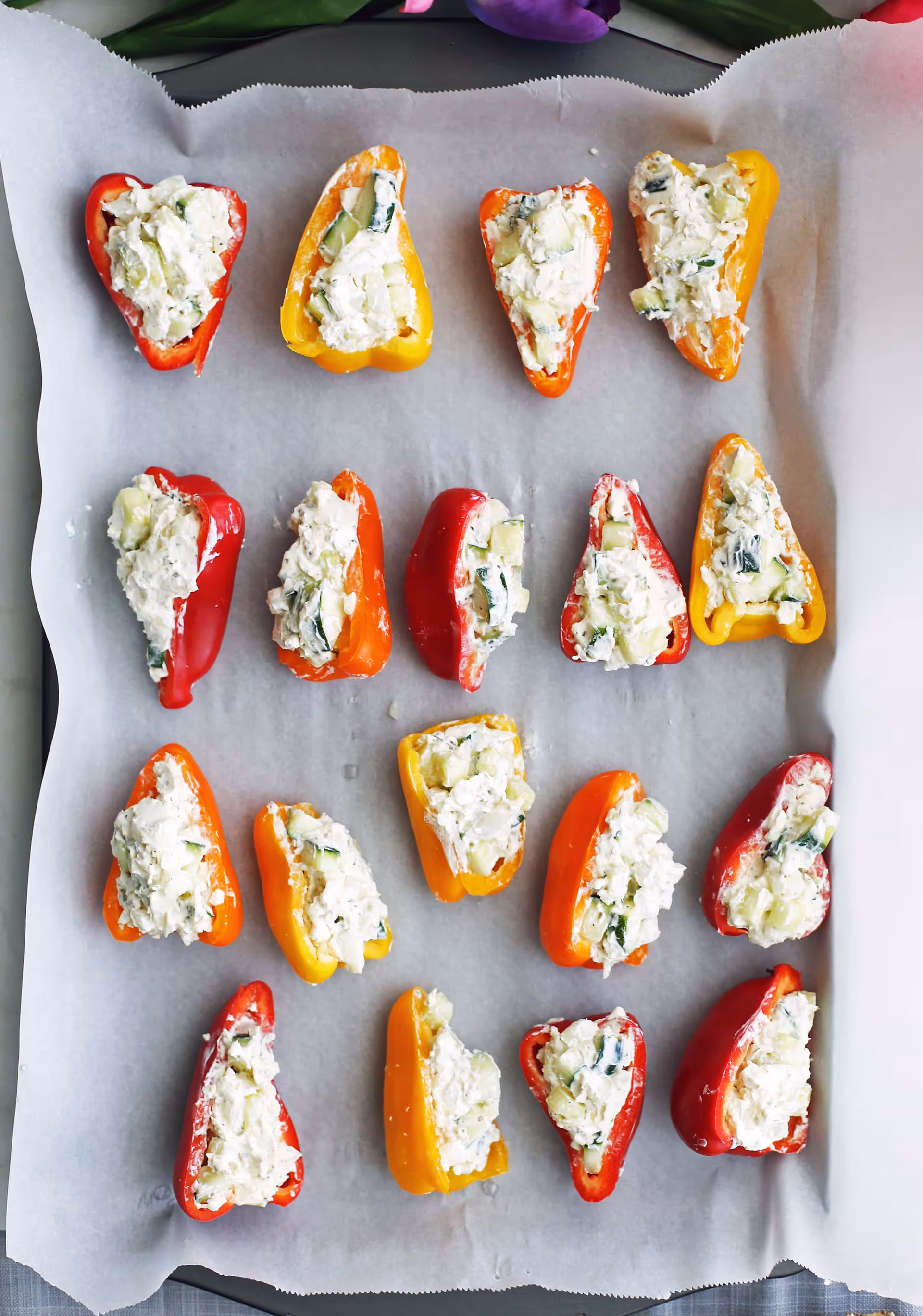 Tray of colorful stuffed peppers on parchment paper in a kitchen.