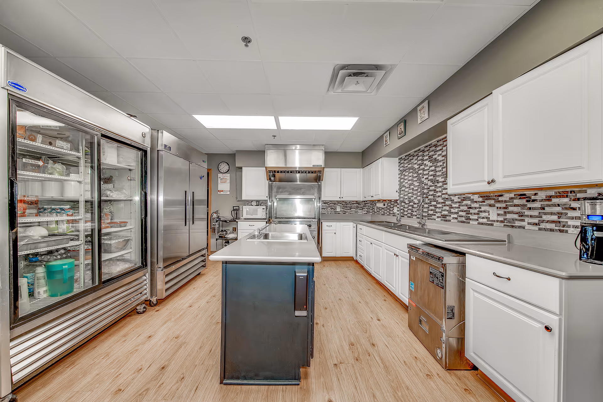 Modern commercial kitchen with white cabinets, stainless appliances, and a central island.