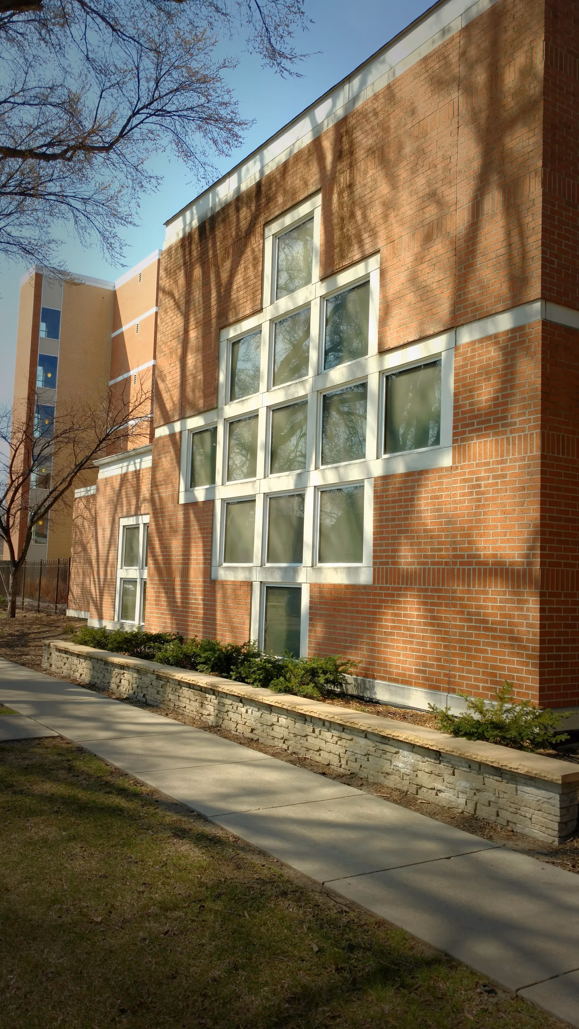 Brick senior living building exterior with large windows and a sidewalk bordered by low stone planters.
