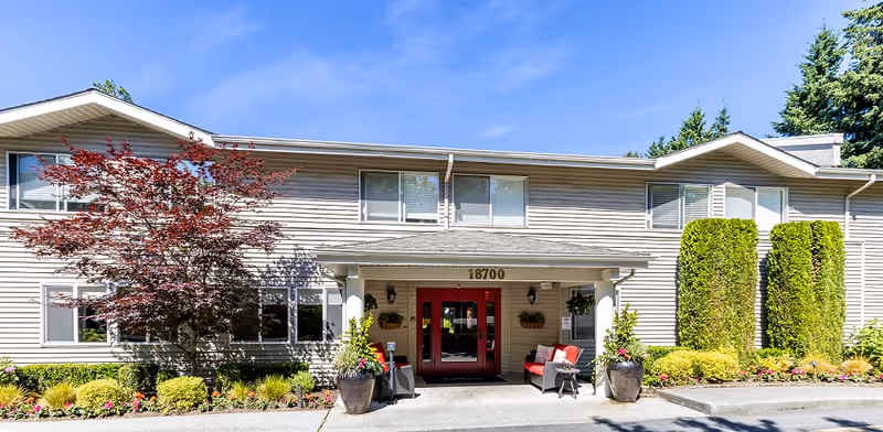 Front entrance of a two-story building with red double doors, address 18700, decorative planters and landscaped beds.