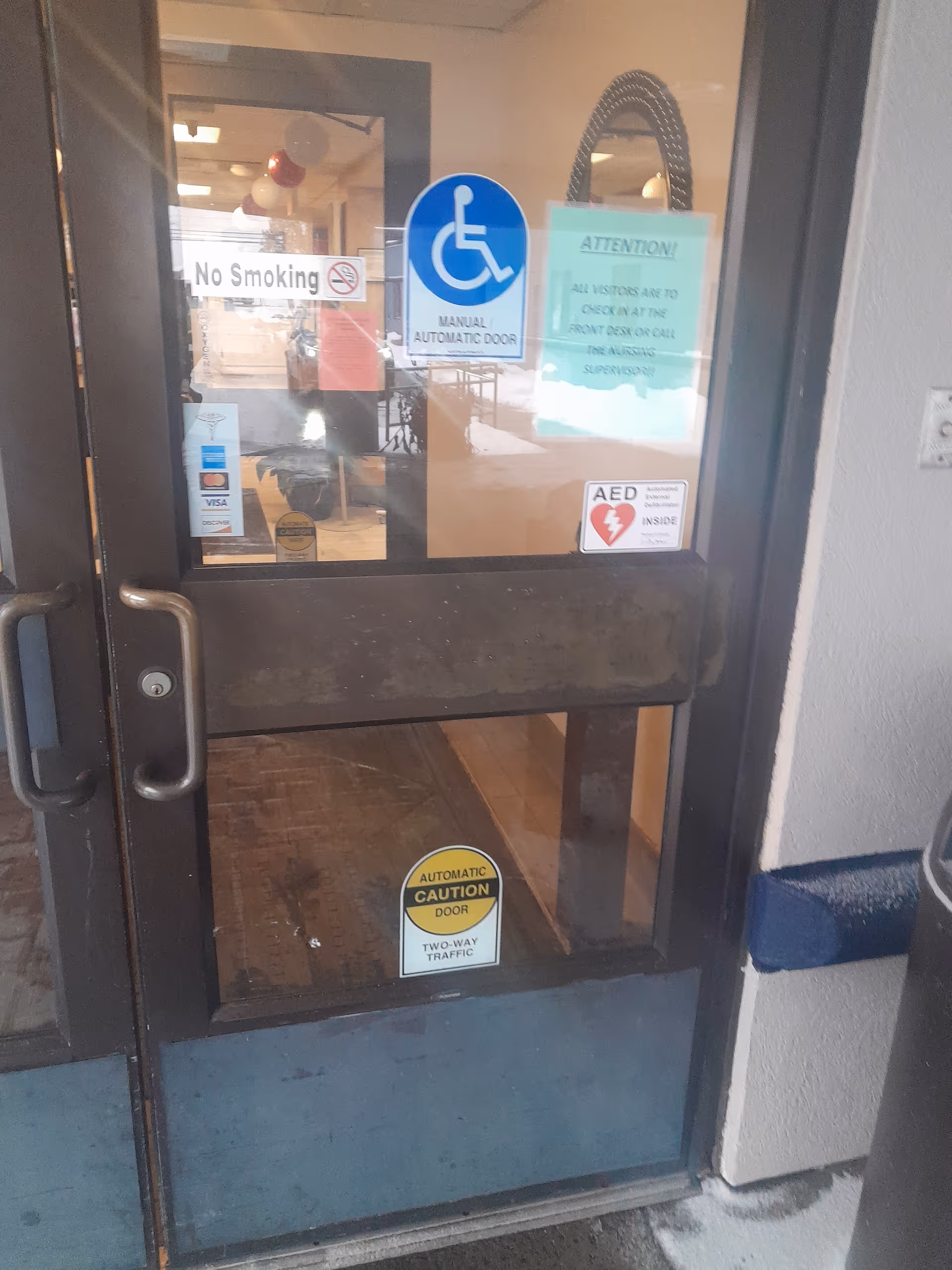 Glass entrance door to Harris Hill Nursing Facility; handicap sign and notices visible.
