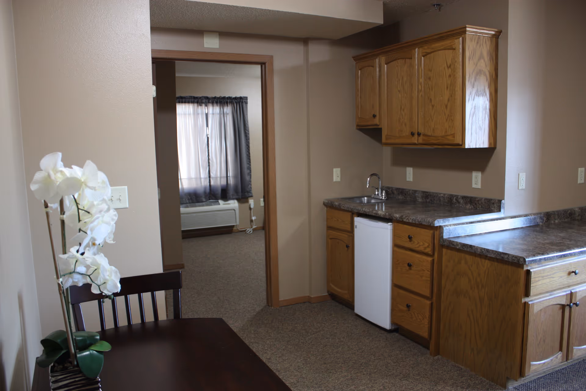 Kitchen area with wooden cabinets, counter, sink, small fridge, and dining table.