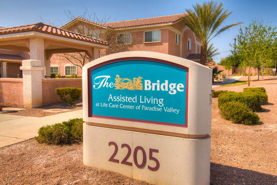 Sign for The Bridge Assisted Living at Life Care Center of Paradise Valley in front of the facility building and landscaped grounds.