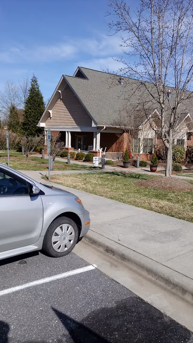Exterior view of a senior living facility with a parked car and landscaped entrance.