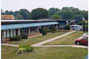 Single-story senior living facility front with a covered walkway, grassy courtyard, and parked vehicles.