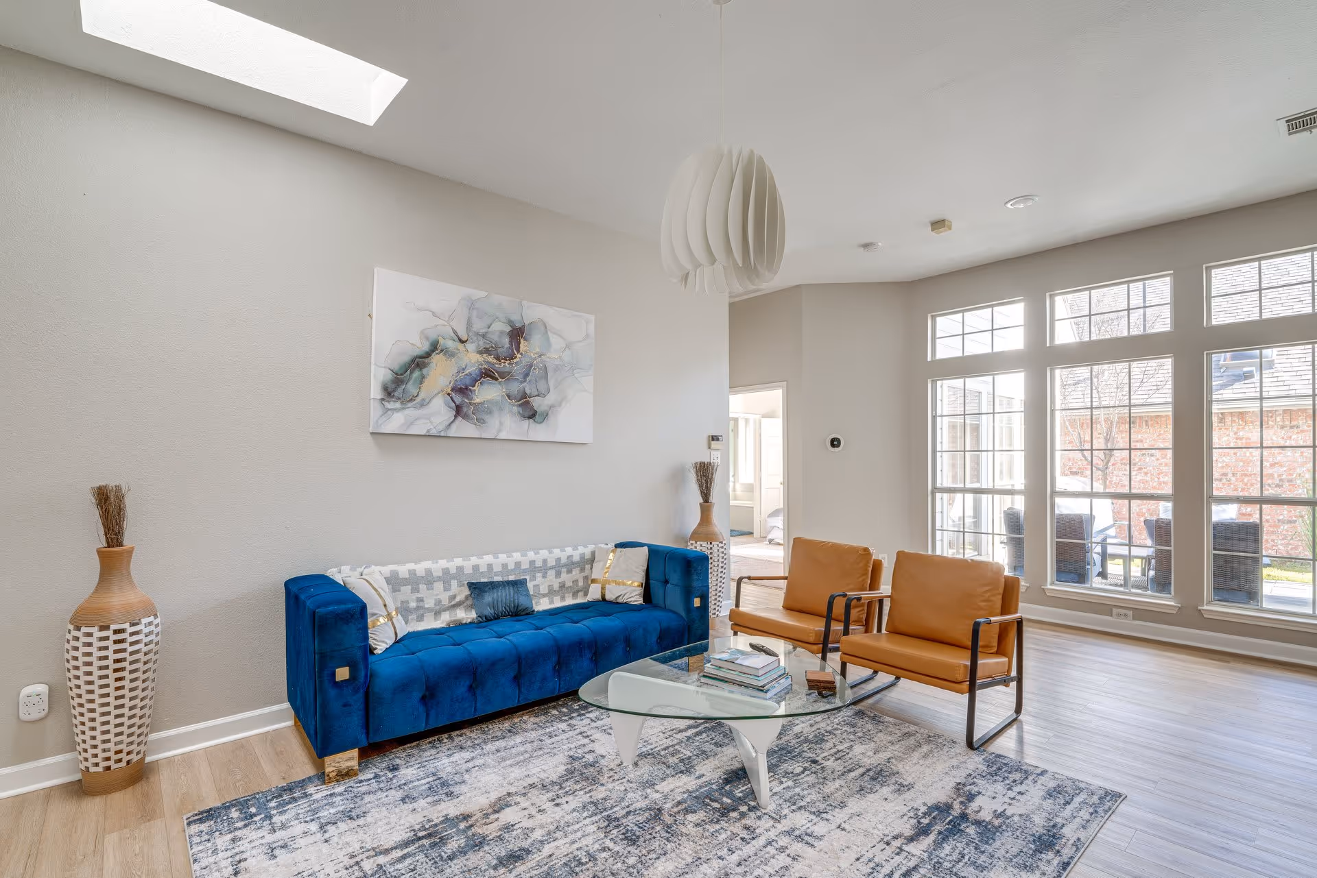 Bright lounge area with blue sofa, brown chairs, glass coffee table, and large windows.