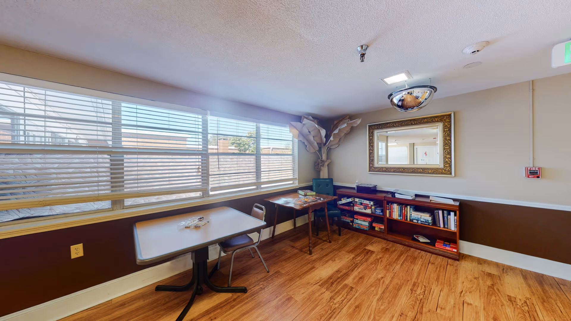 Bright common room with large windows, a table, chairs, and a bookcase.