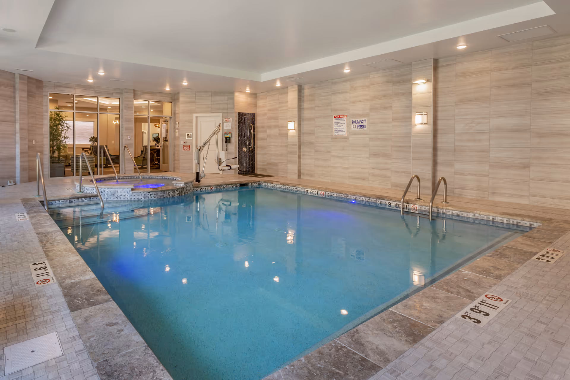 Indoor pool area with a spa, tiled walls, and a glass doorway leading to a lounge.