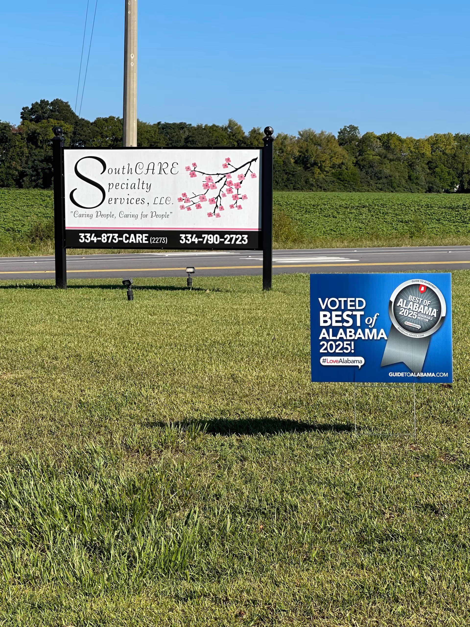 Outdoor grassy area with a large SouthCARE Specialty Services sign beside a blue award sign.