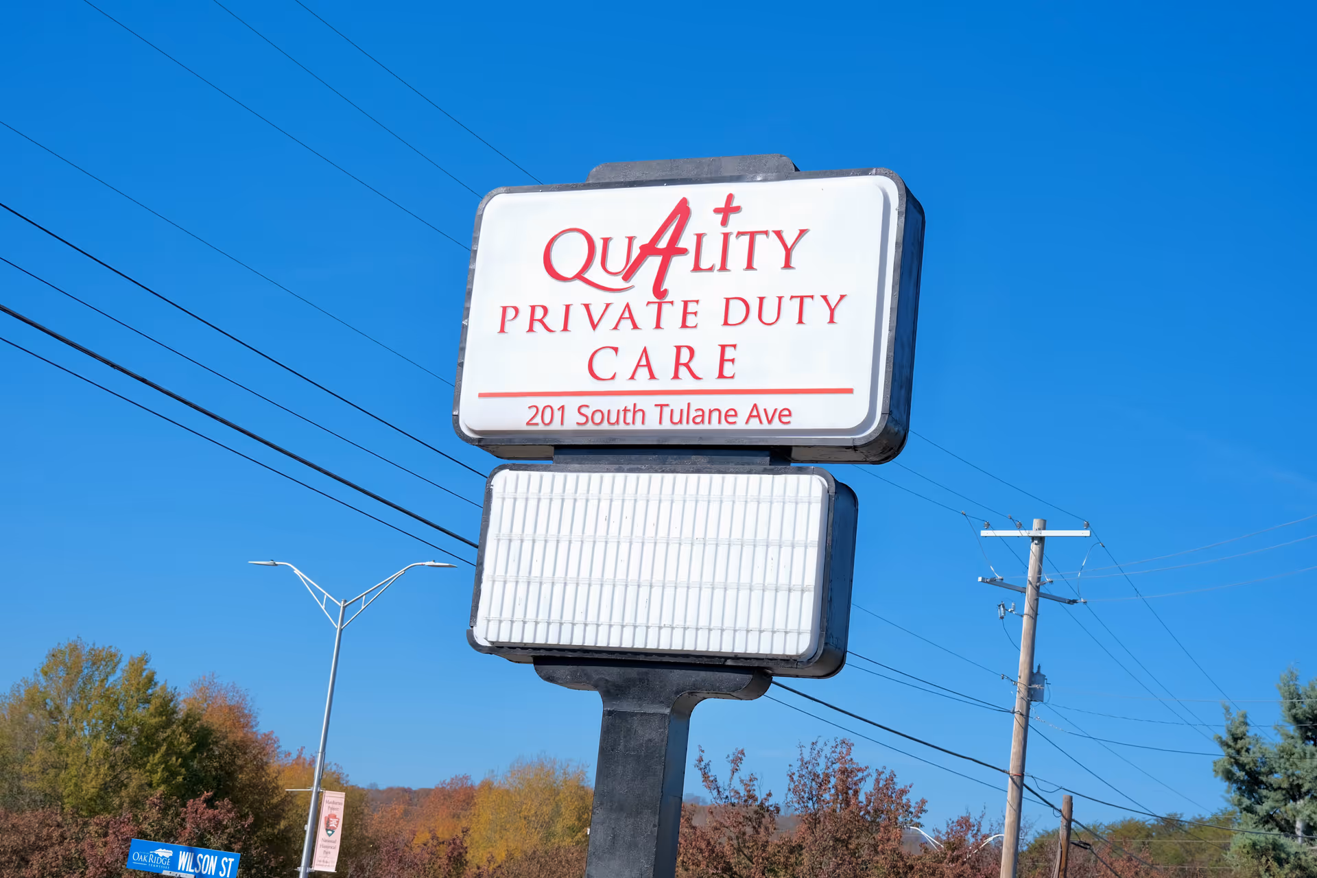 A roadside sign for Quality Private Duty Care against a clear blue sky.