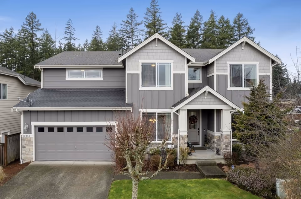 Two-story gray house with attached garage and small front lawn, trees in background.