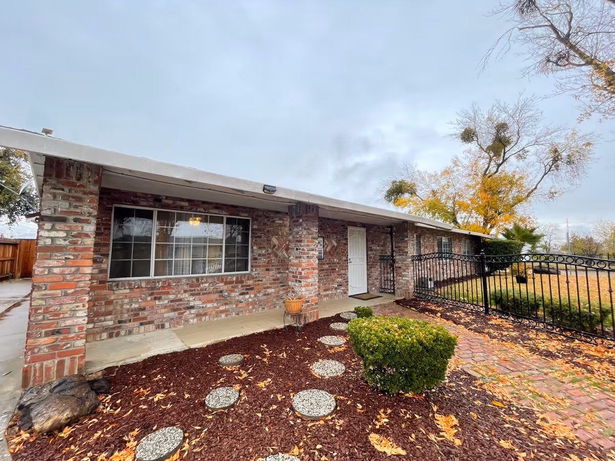 Brick single-story senior care building exterior with walkway, mulch, and autumn leaves.