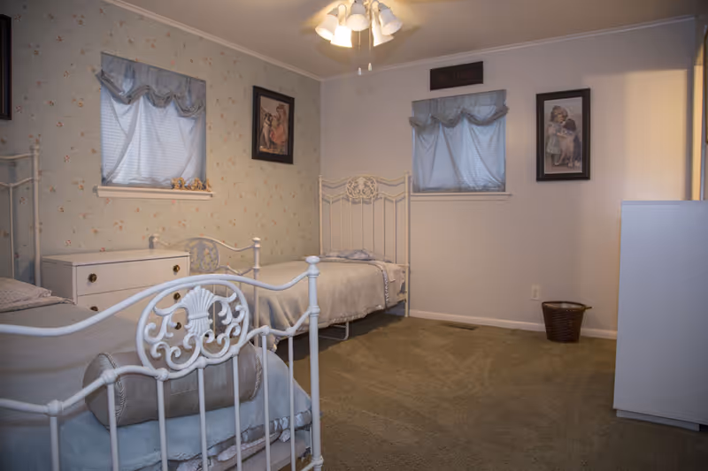 Two white metal beds and dresser in a cozy floral patterned senior living bedroom