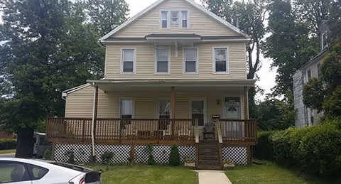 Two-story beige house with a wooden front porch and steps.