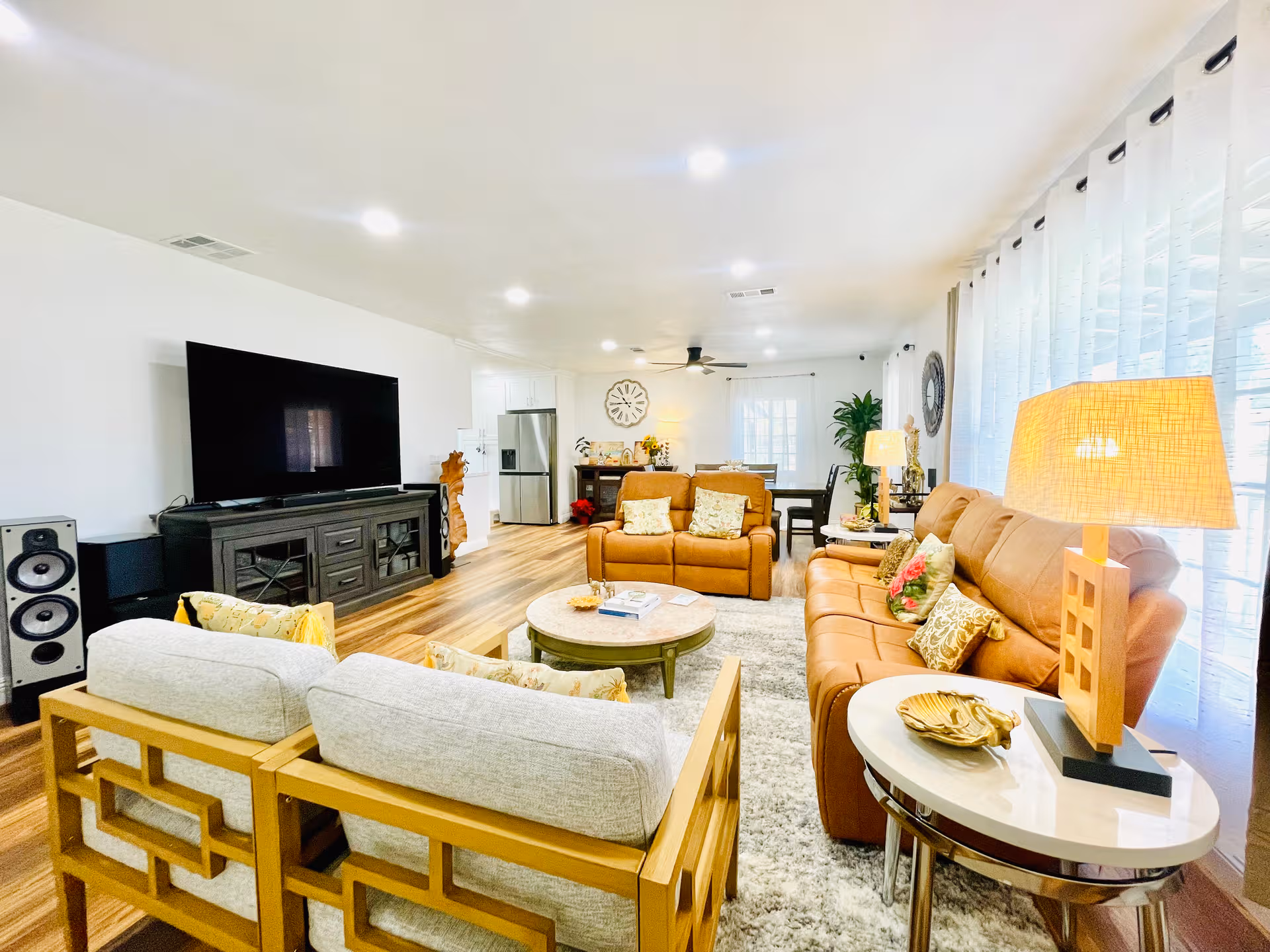 Bright living room with brown leather sofas, grey chairs, and a large TV.
