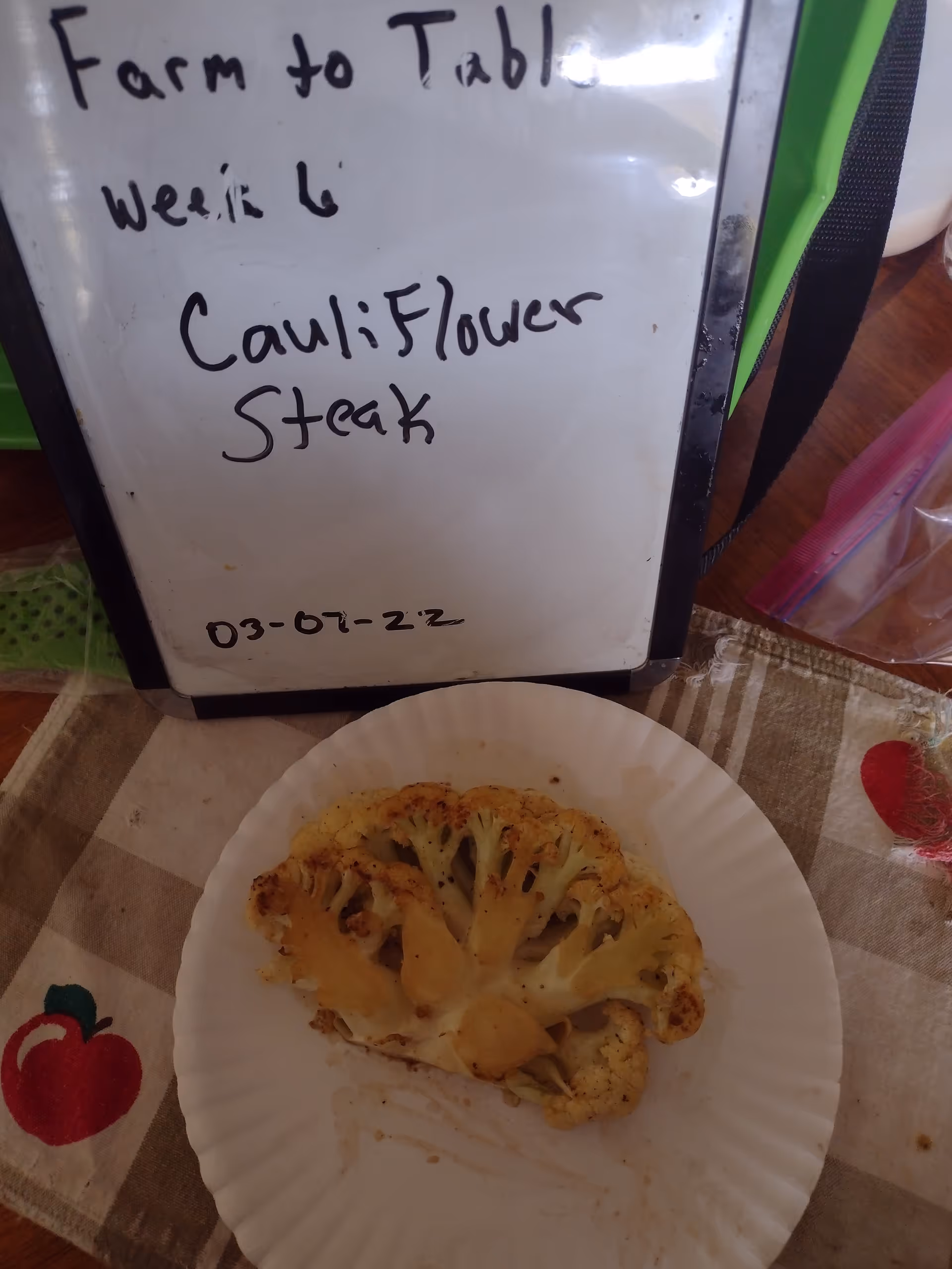 Whiteboard lists Farm to Table week and cauliflower steak beside a roasted cauliflower on a plate.