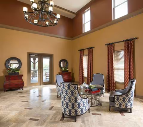 A spacious interior lounge with patterned chairs, a chandelier, and windows overlooking an outdoor patio.