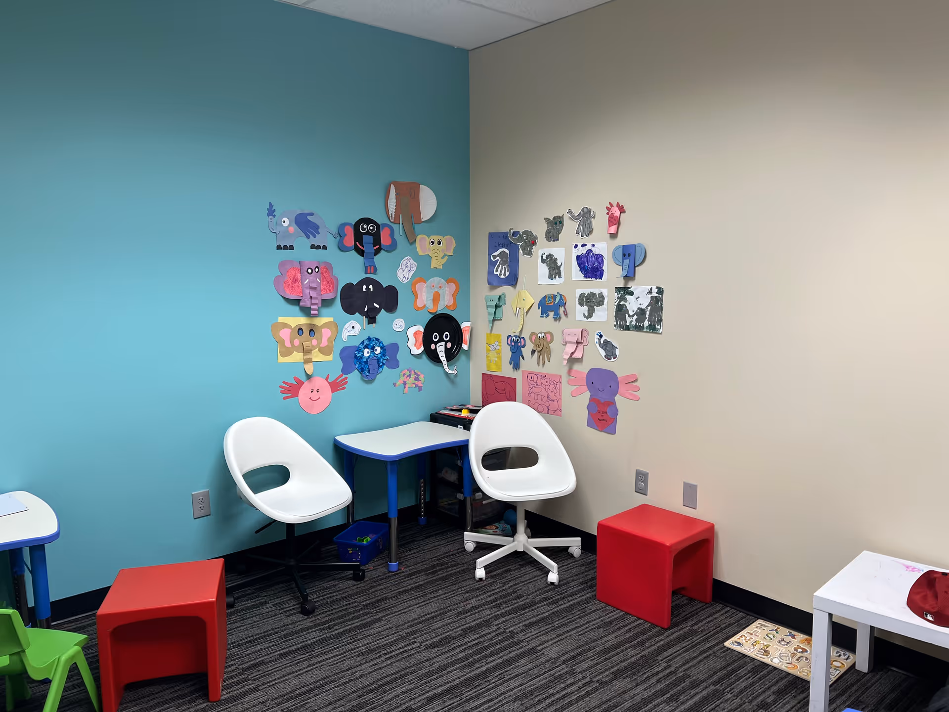Colorful children's art displayed on teal and beige walls in a small play corner.