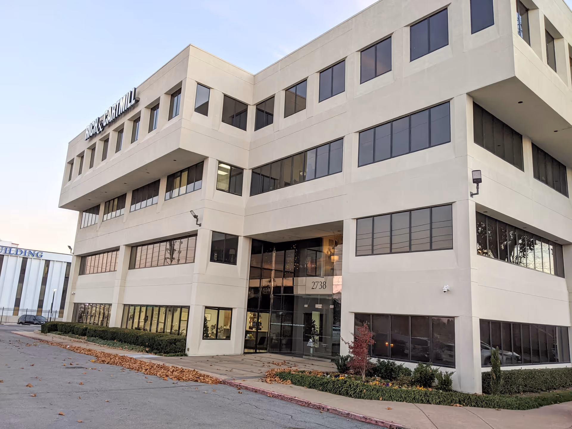 Modern beige, multi-story building with glass entrance and landscaping.