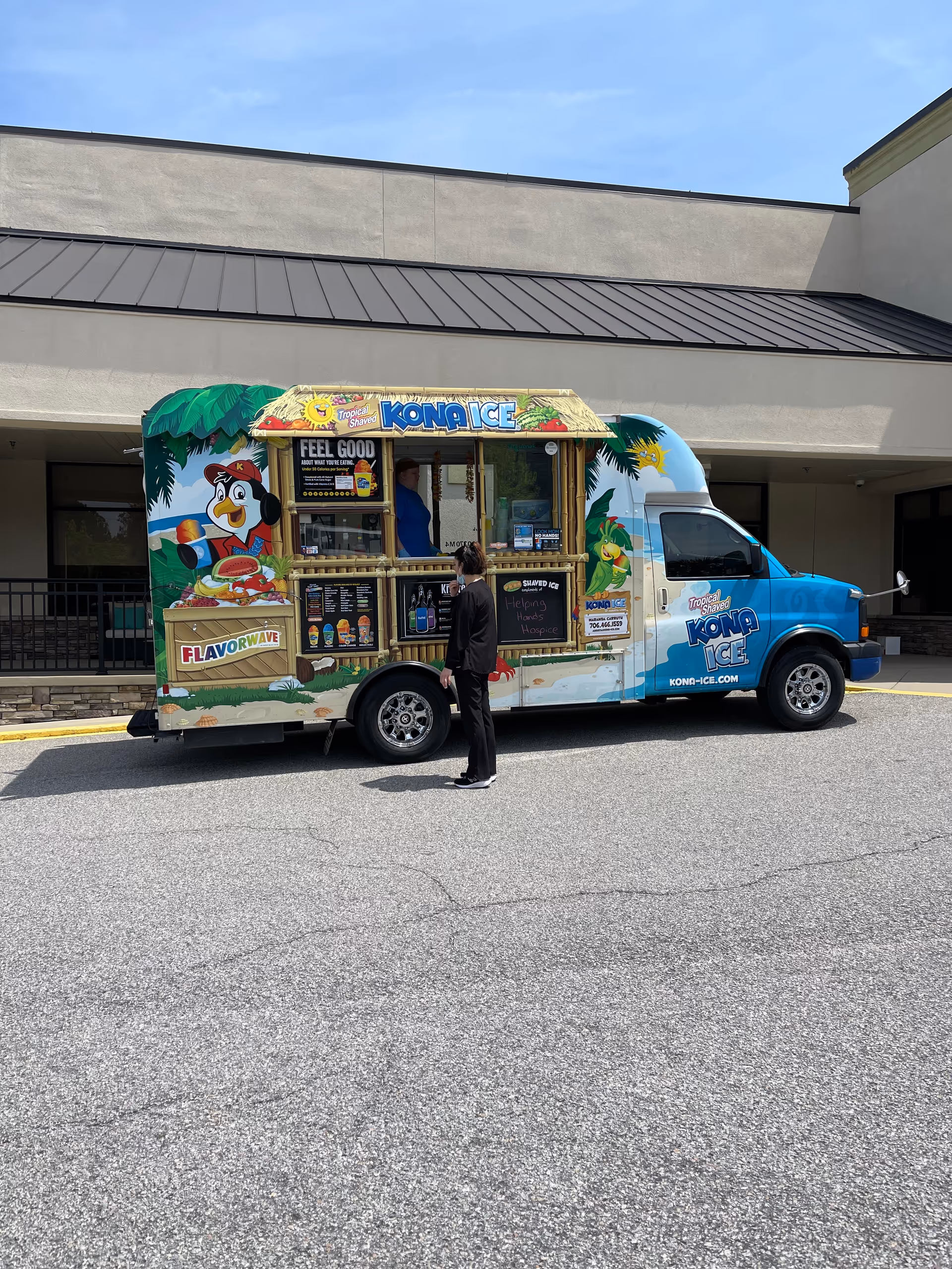 Kona Ice truck parked outside Helping Hands Hospice with two people nearby