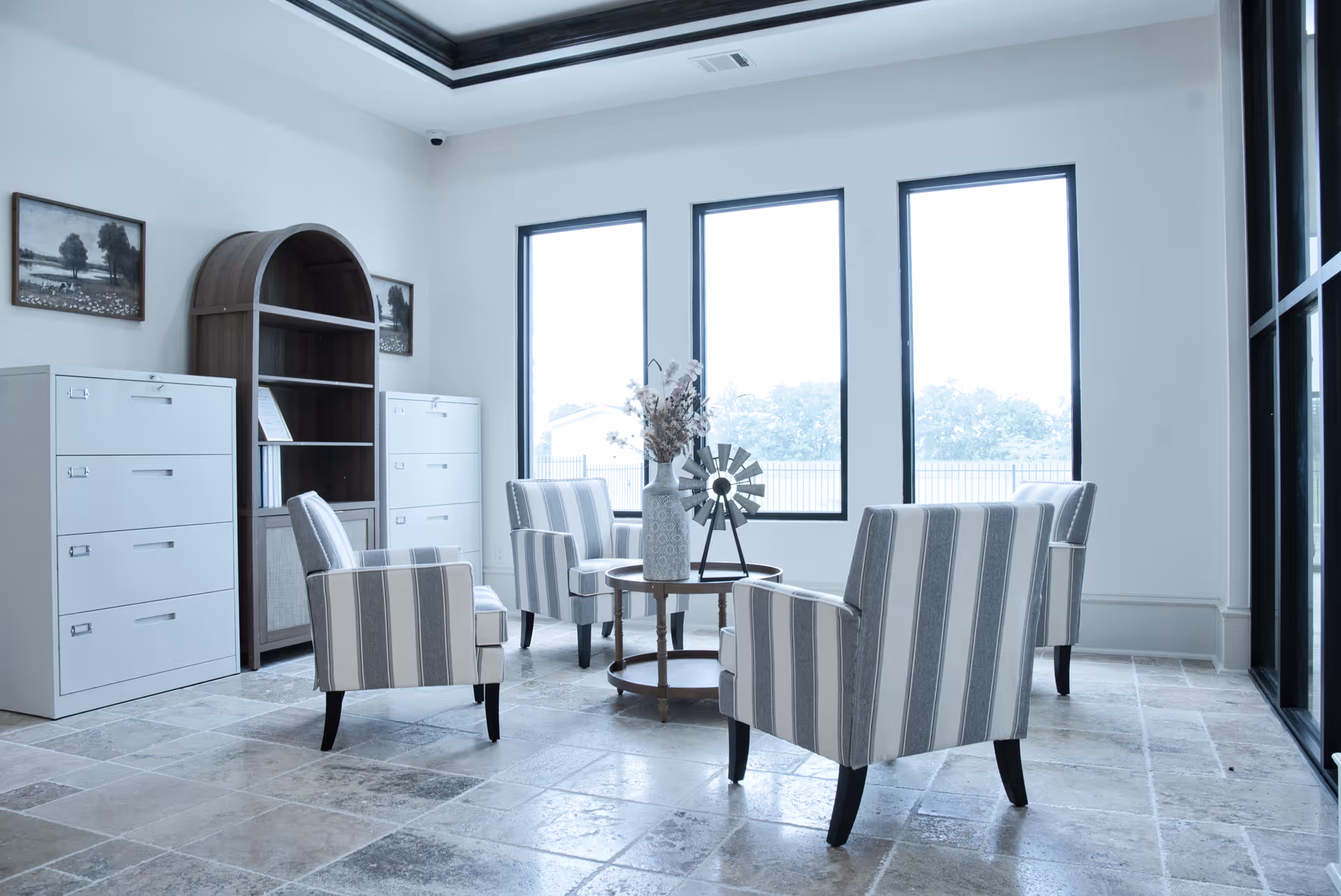Bright modern lounge with striped armchairs, a round table, and large windows.