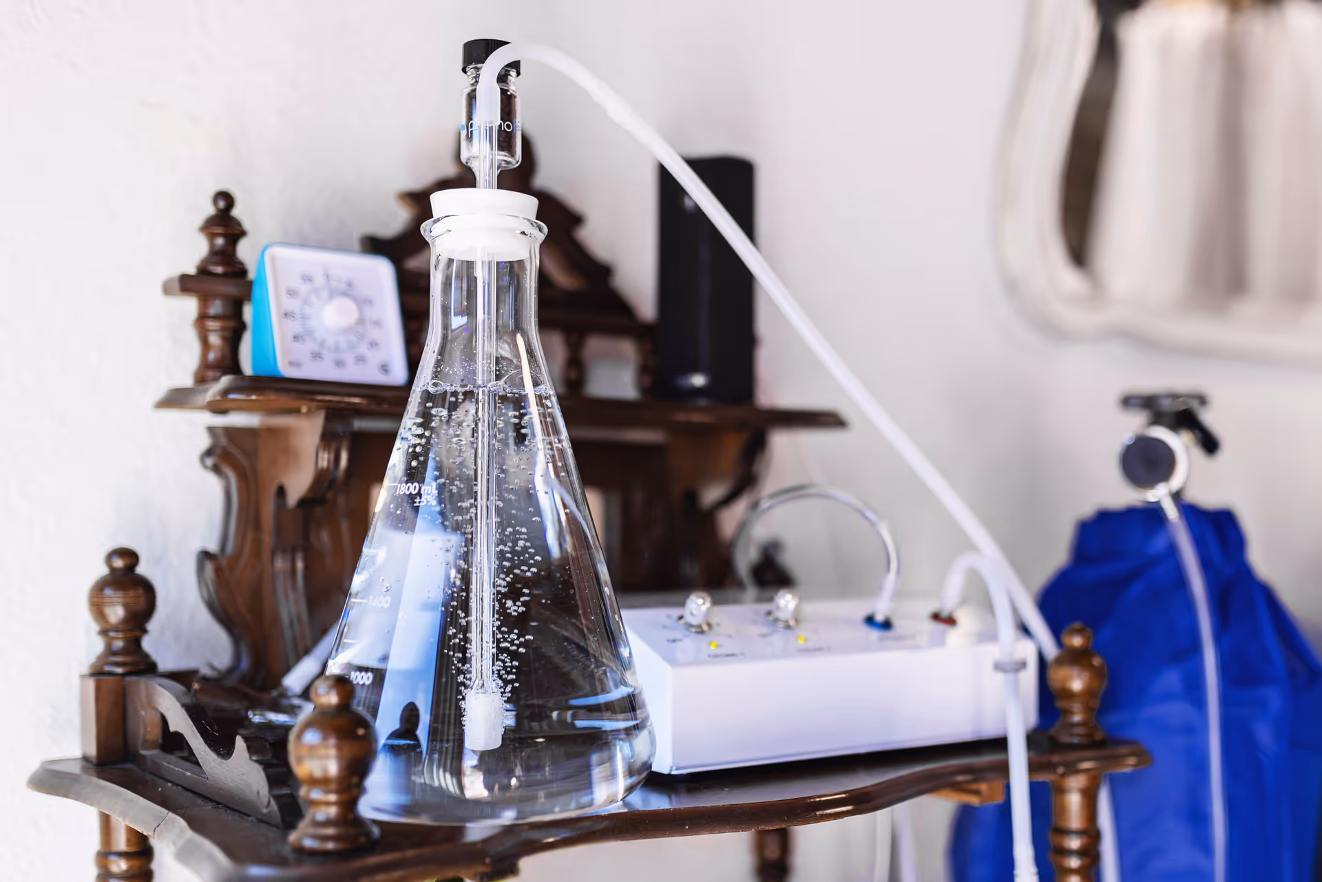 Clear Erlenmeyer flask connected to tubing and a control unit on a wooden stand.
