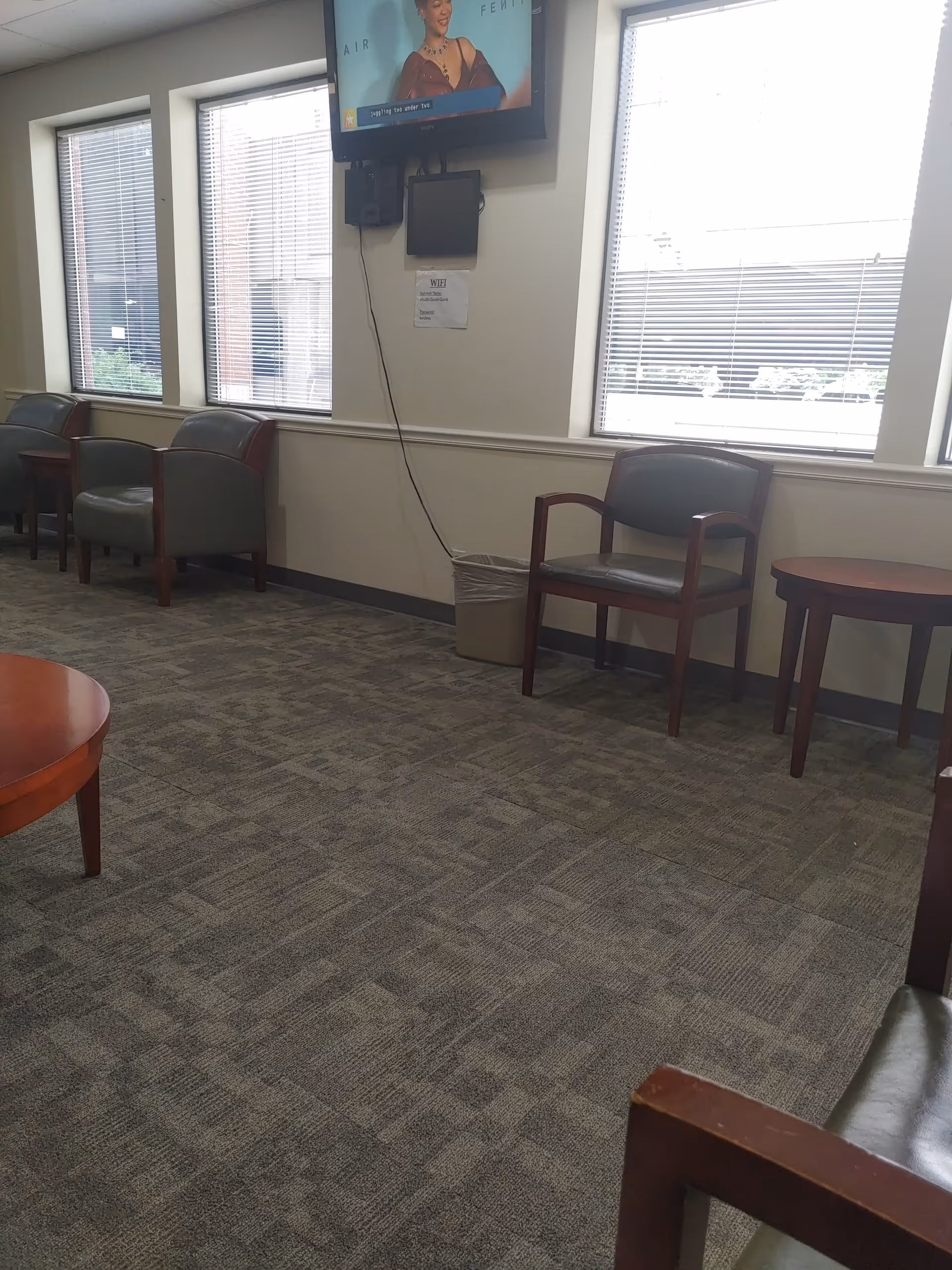 Waiting room with chairs, small tables, blinds, and a wall-mounted TV.