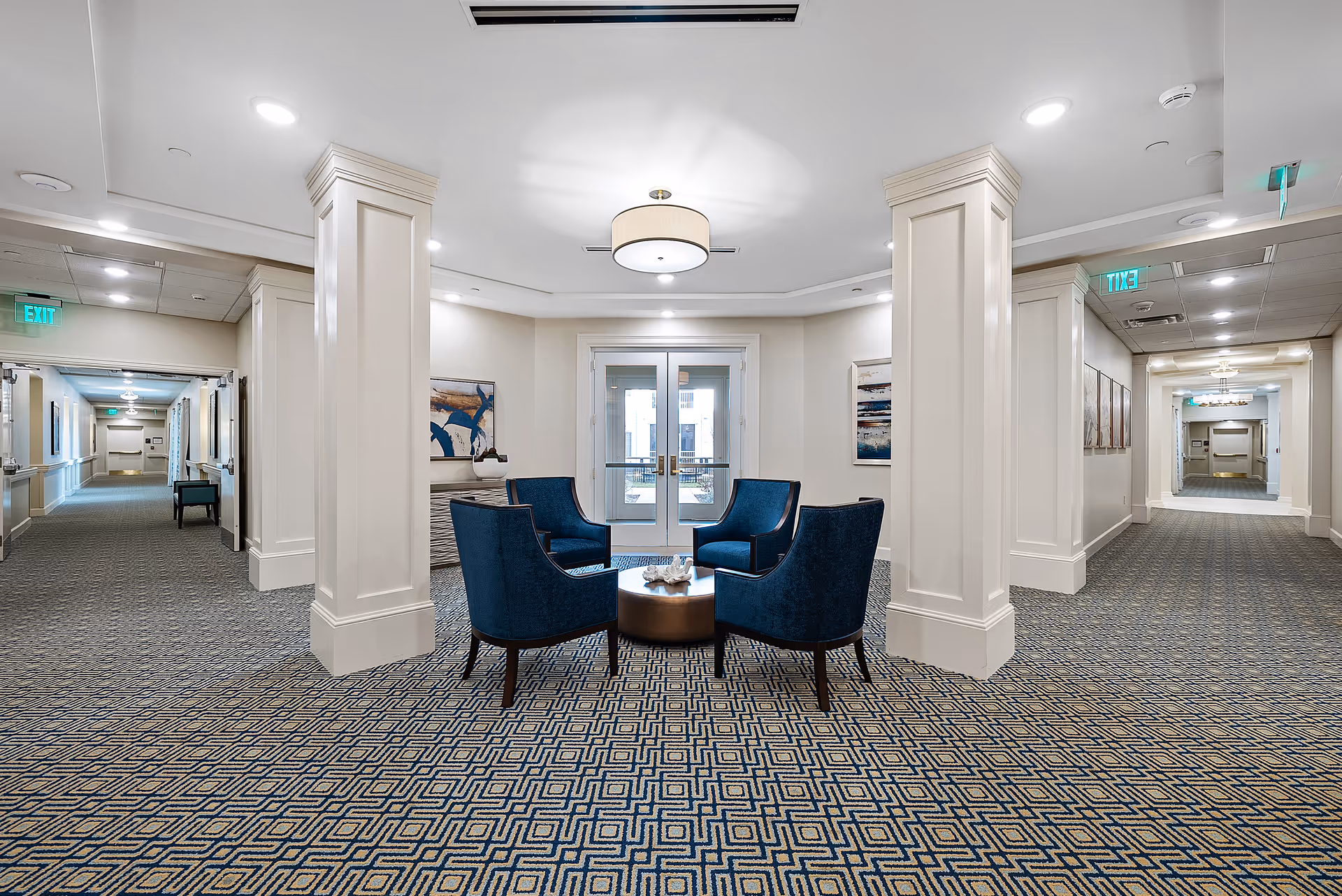 Bright central lounge in a senior living facility with blue chairs around a circular table.