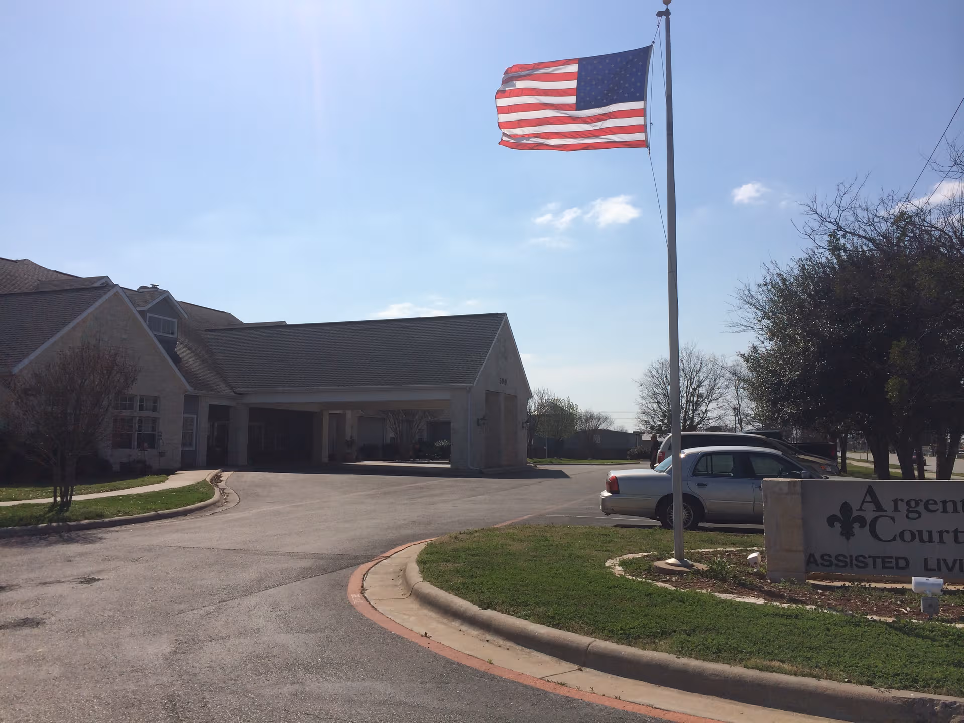 Exterior view of Argent Court Assisted Living with flagpole, entrance, and parked cars.