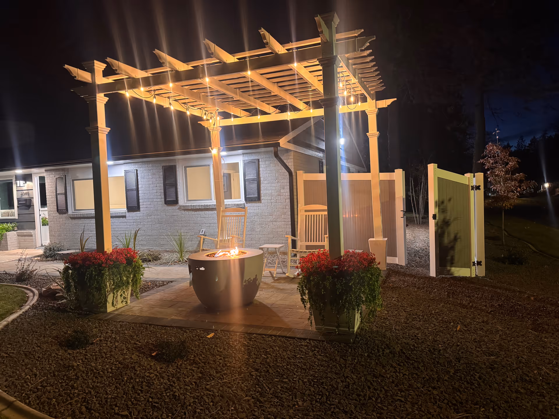 Night exterior view of Cozy Villa Adult Family Home with lit pergola, fire pit, and seating.