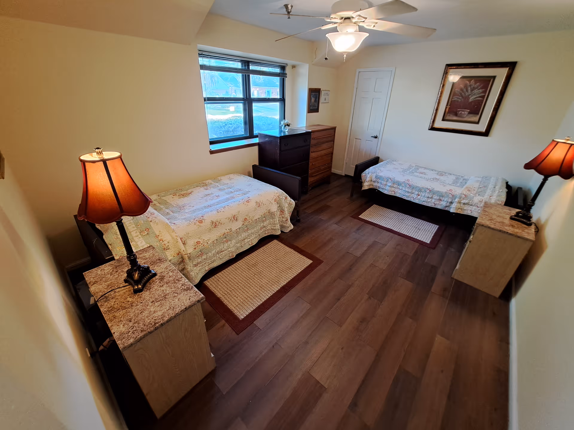 Two twin beds with dressers, lamps, and a ceiling fan in a bedroom.