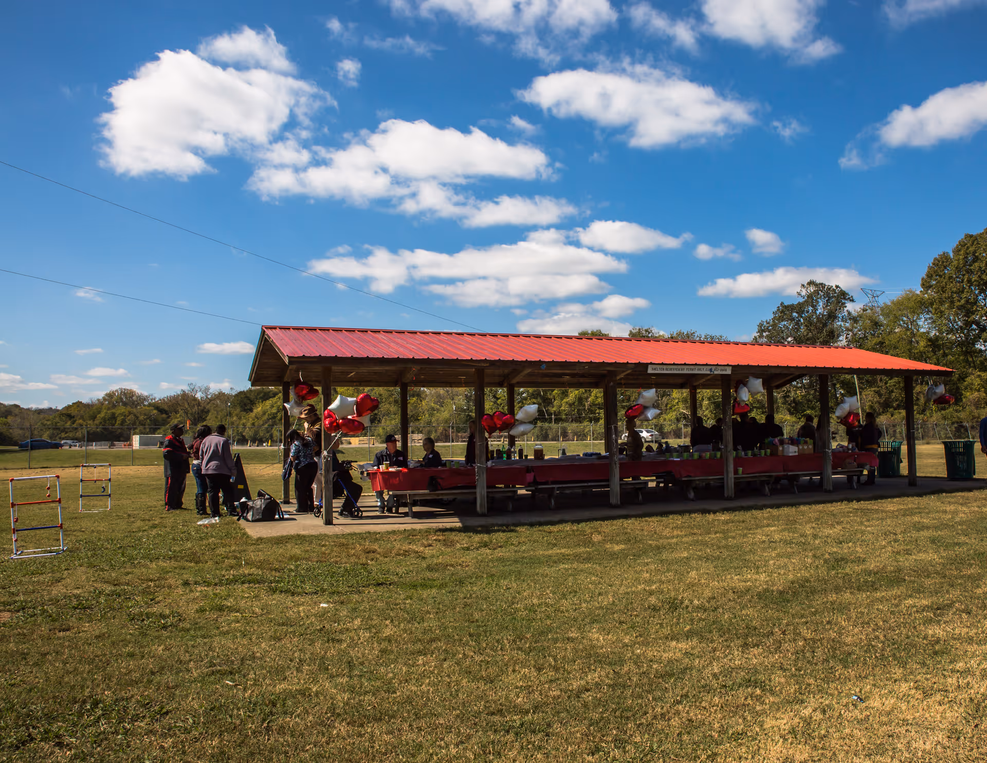 Outdoor pavilion with people gathered around a long table under a red roof.