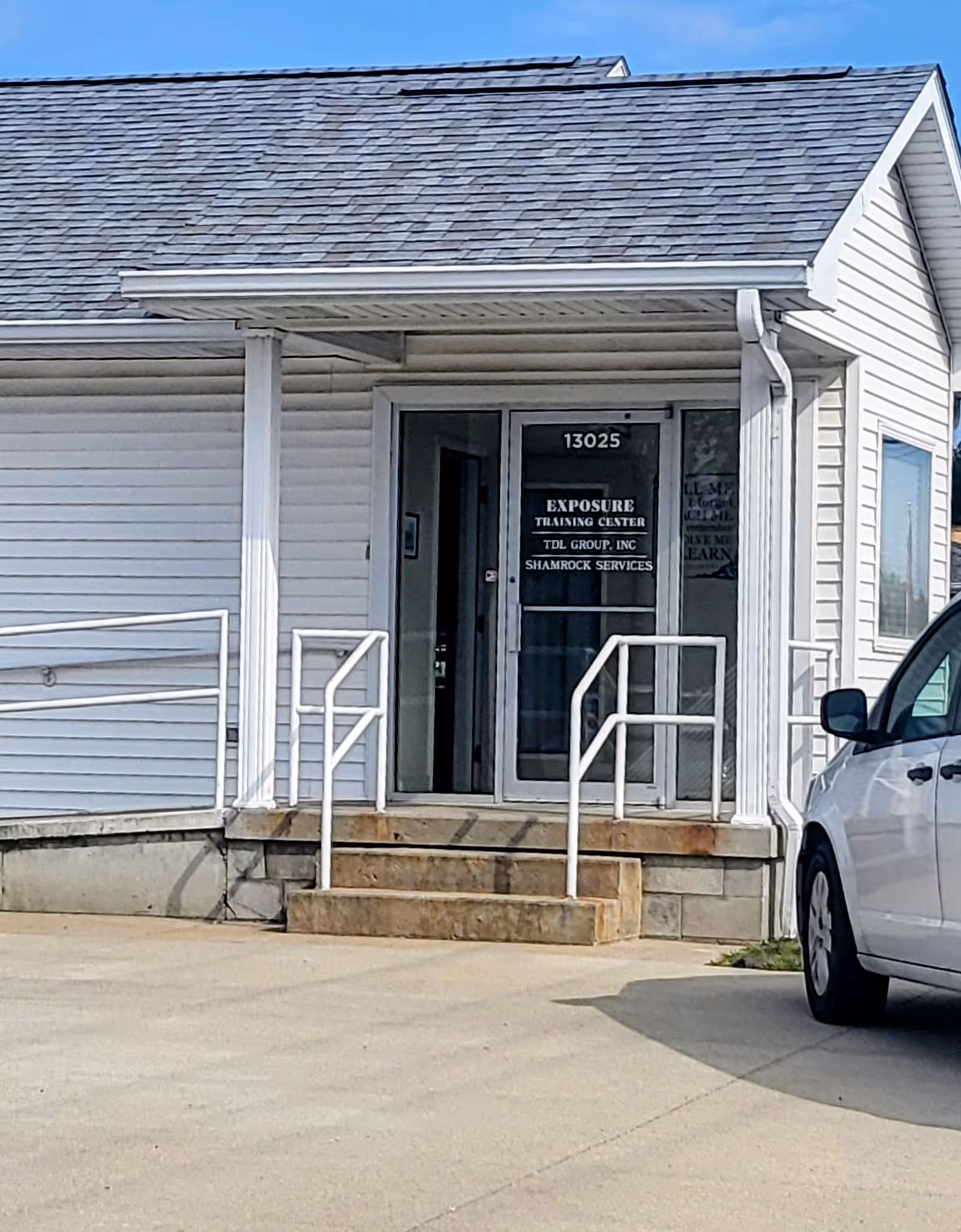Exterior view of a white facility entrance with steps and metal railing.