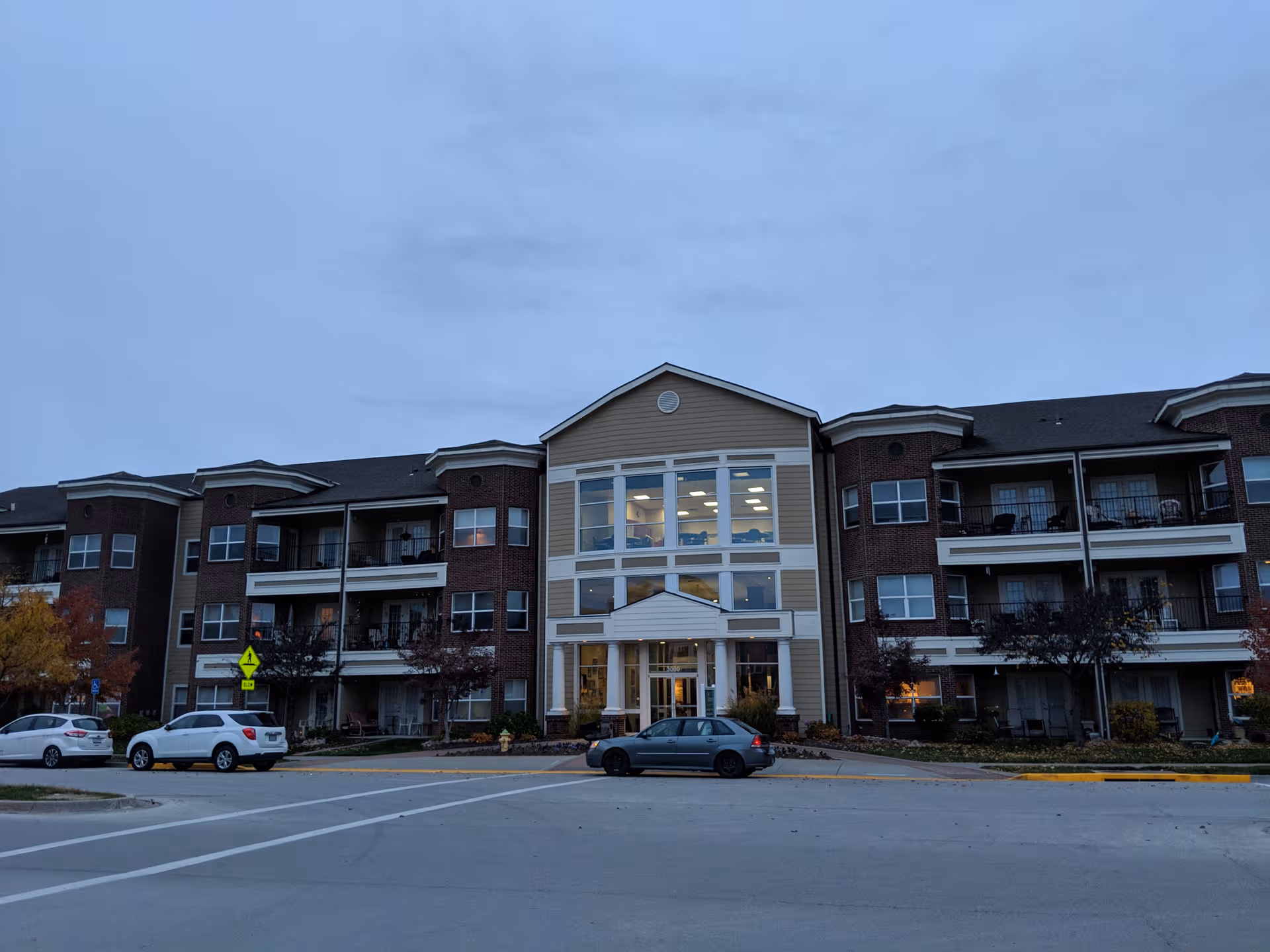 Multi-story senior living building with a central glass entrance and parking lot.