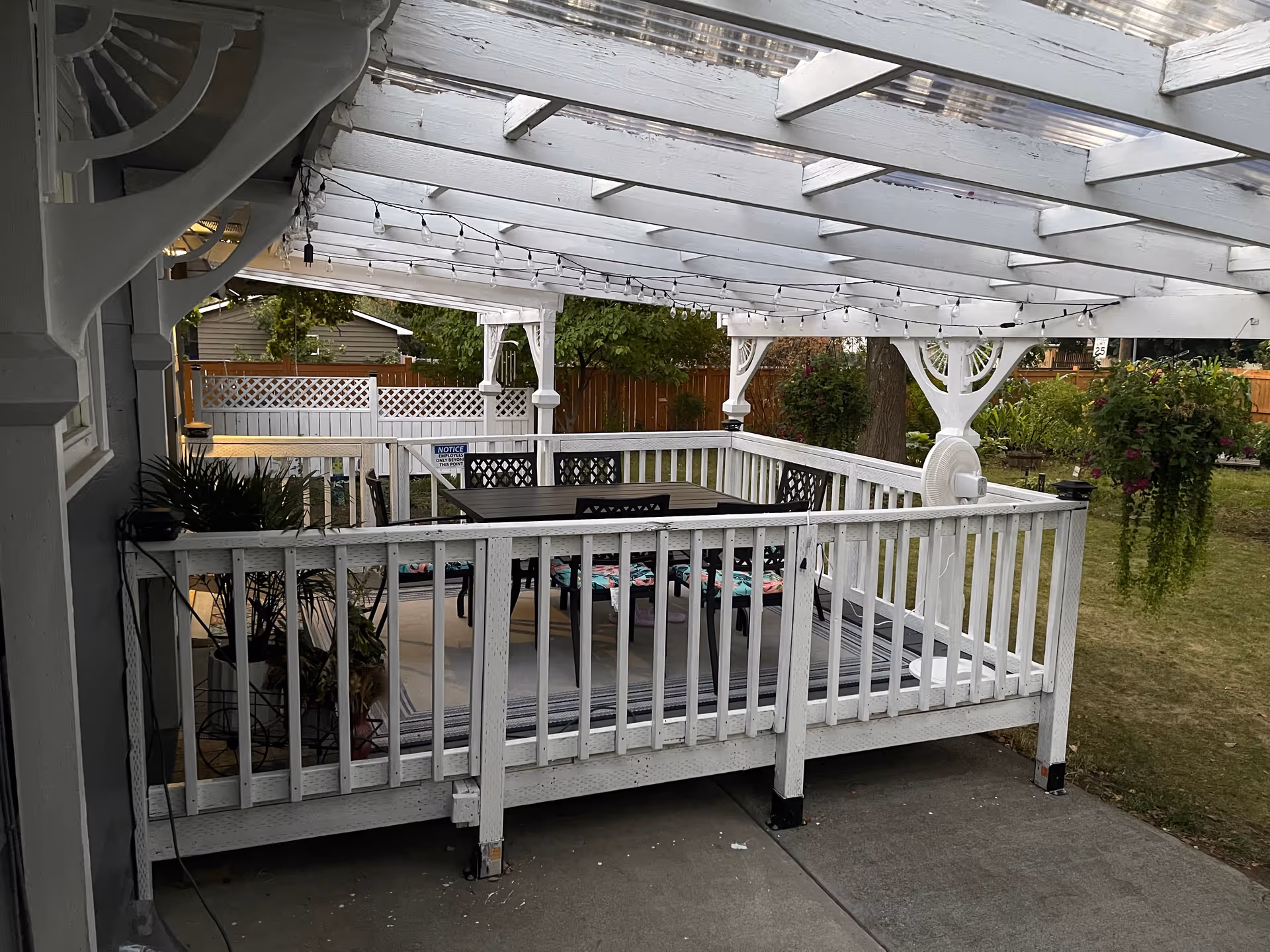 White wooden deck with a table, chairs, and string lights under a pergola.