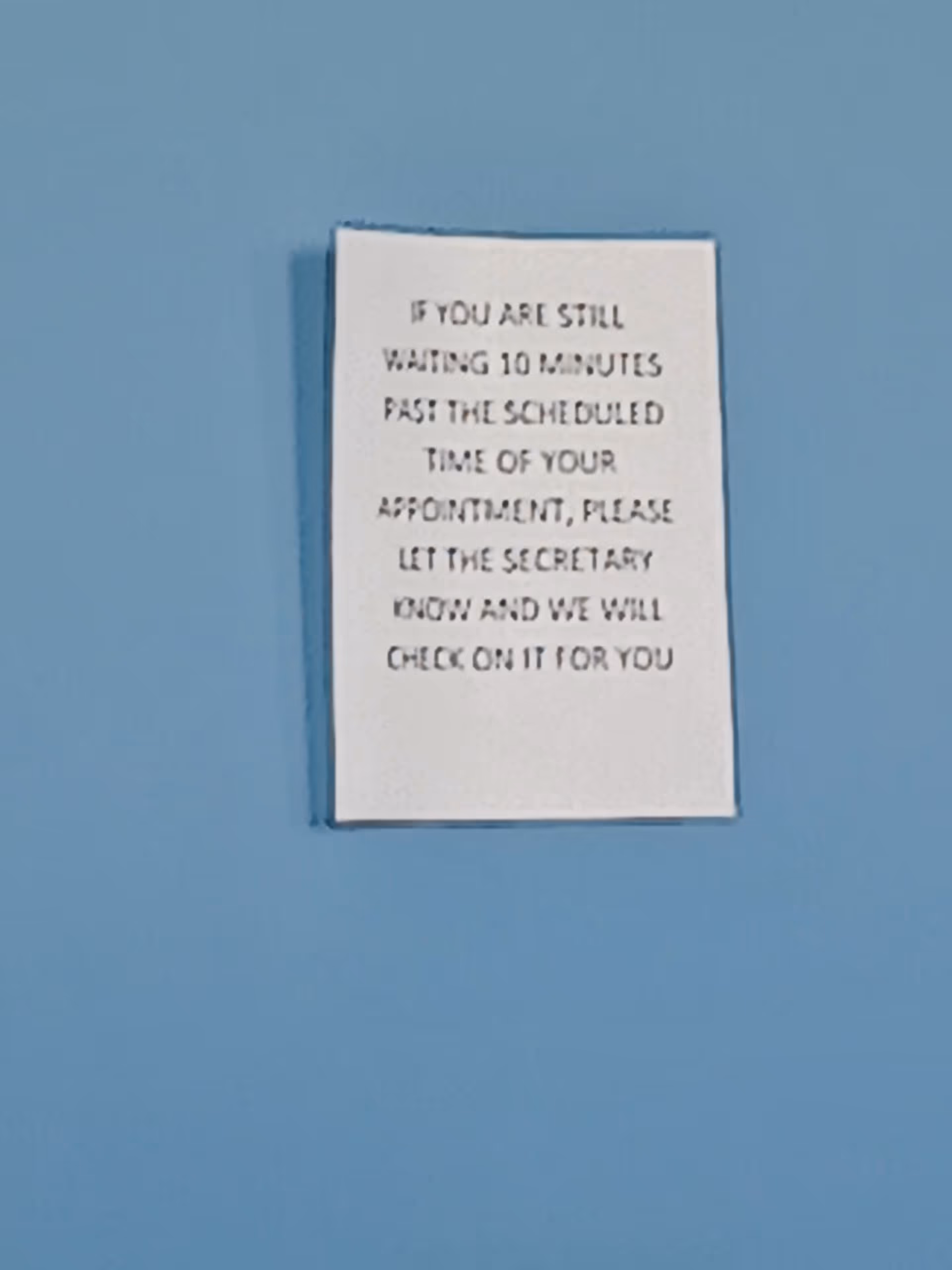 White sign on blue wall displaying appointment reminder text.